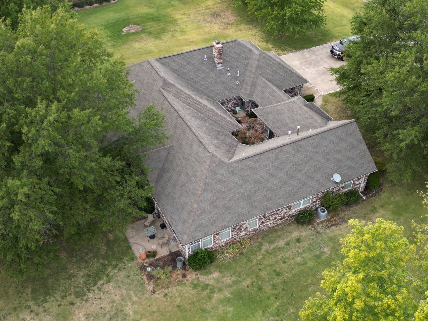 An aerial view of a house with a roof that is surrounded by trees.