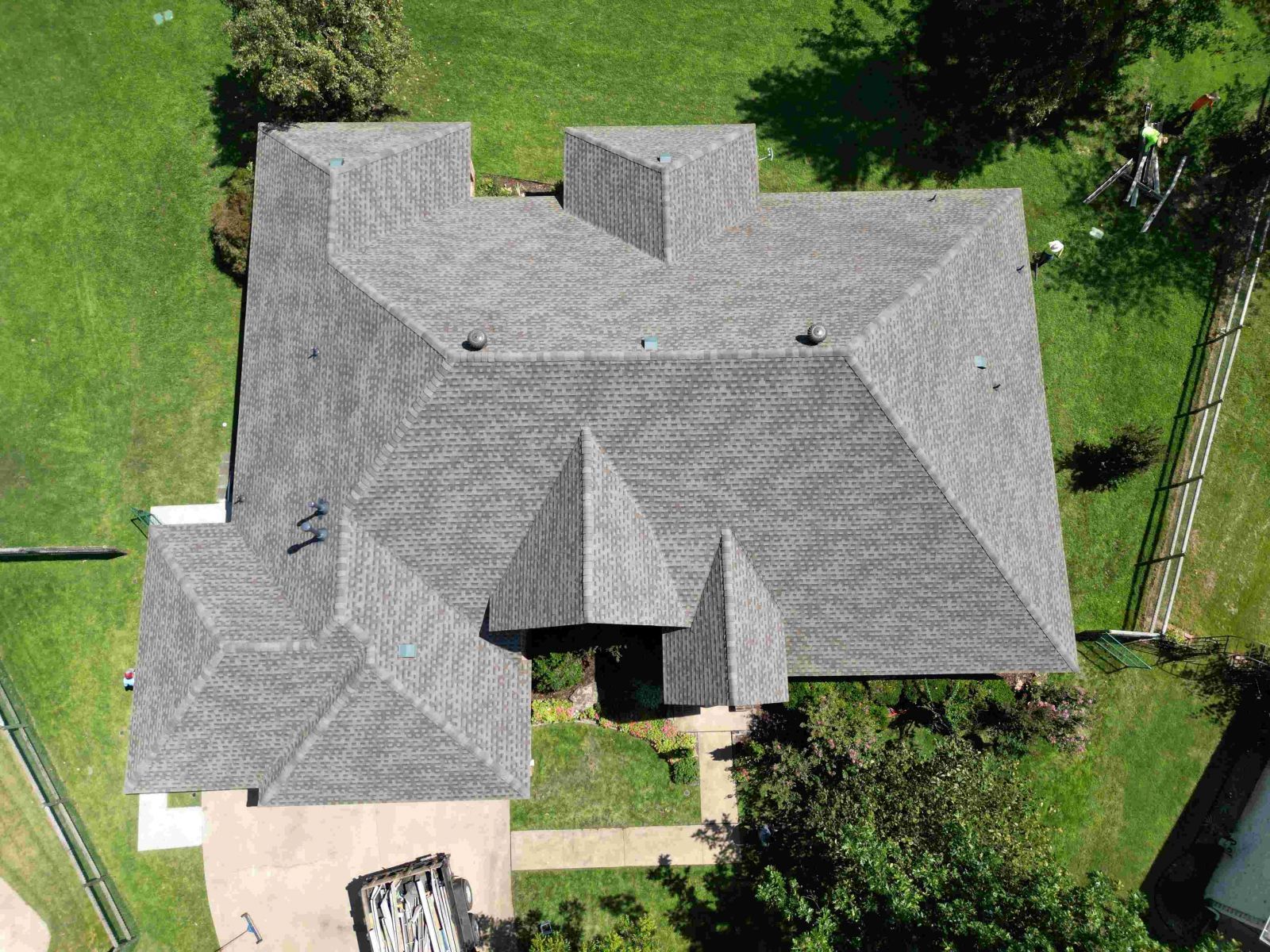 An aerial view of a large house with a gray roof surrounded by grass and trees.