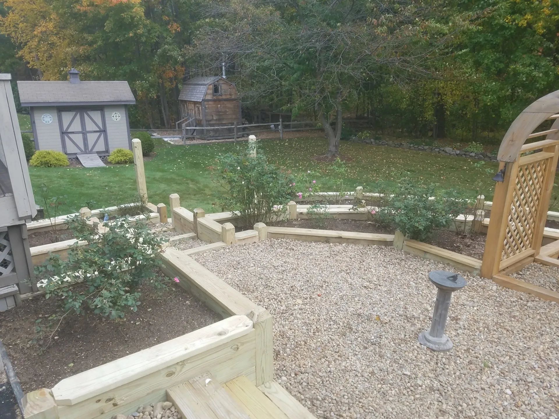 Backyard garden with gravel path, raised flower beds, a small shed, and a trellis arch.