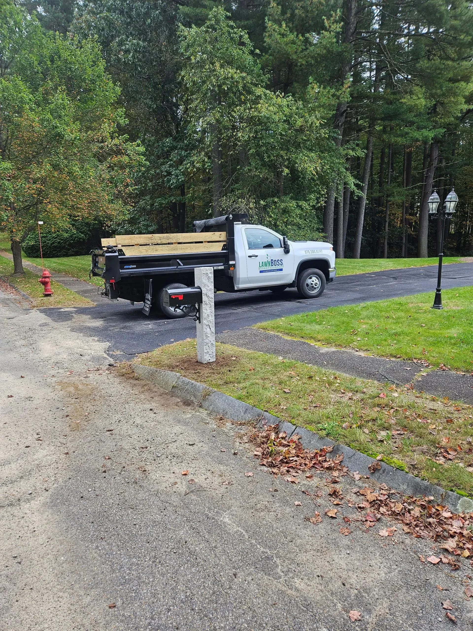 White dump truck on a gravel driveway beside a wooded yard after rain