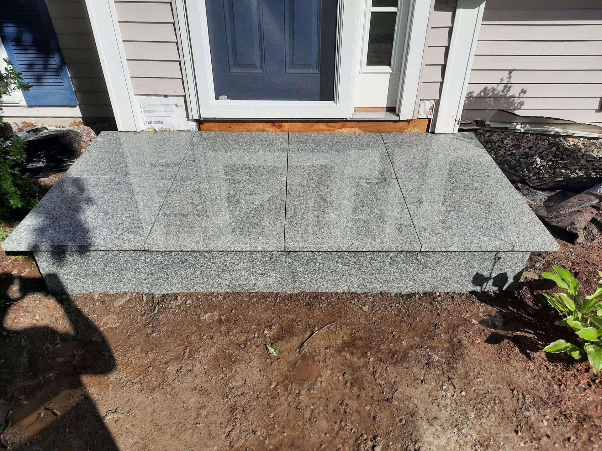 Freshly poured gray concrete front step in front of a house door, with bare dirt surrounding it.