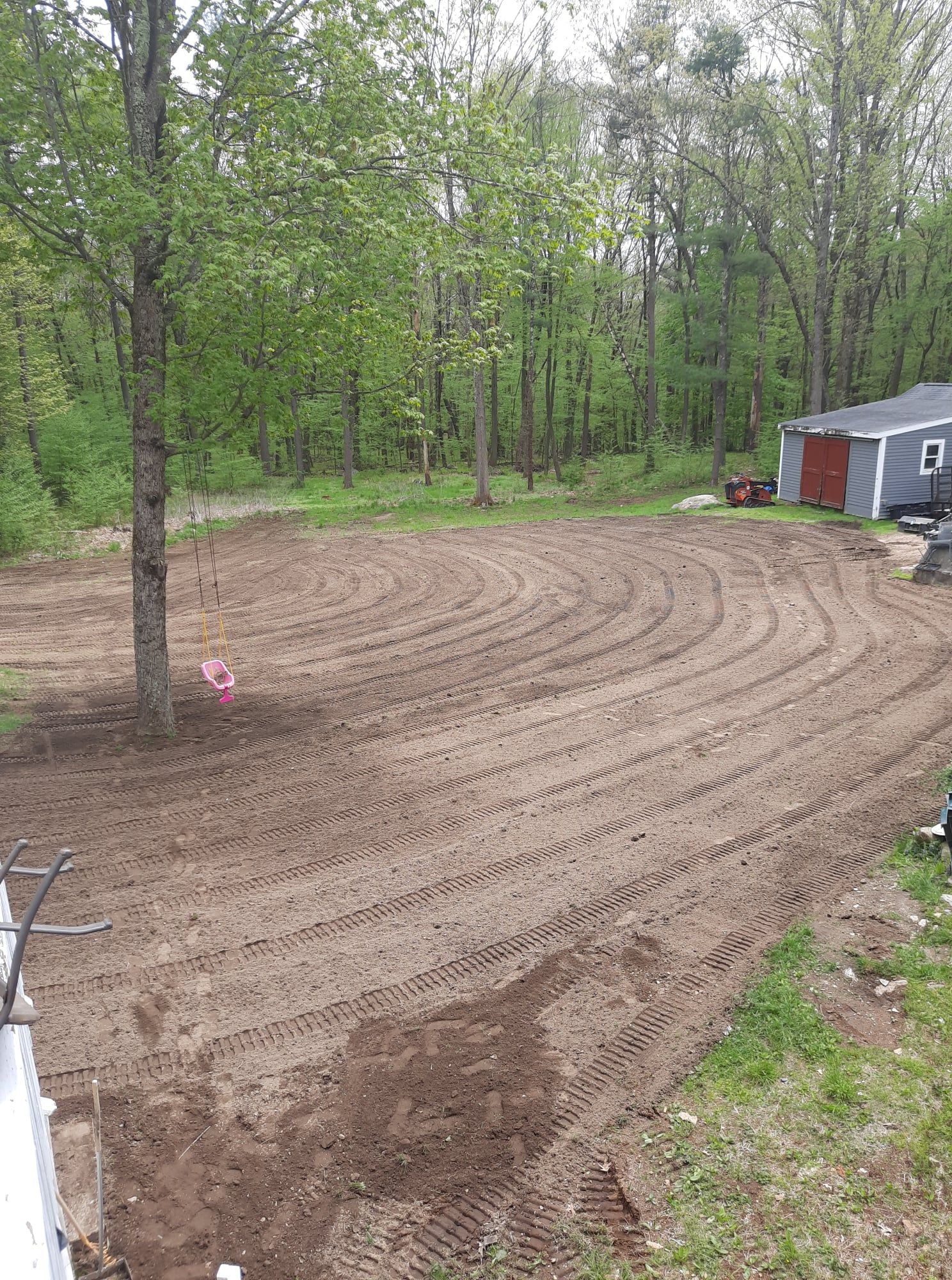 Freshly tilled dirt in a yard beside a shed, with trees in the background.
