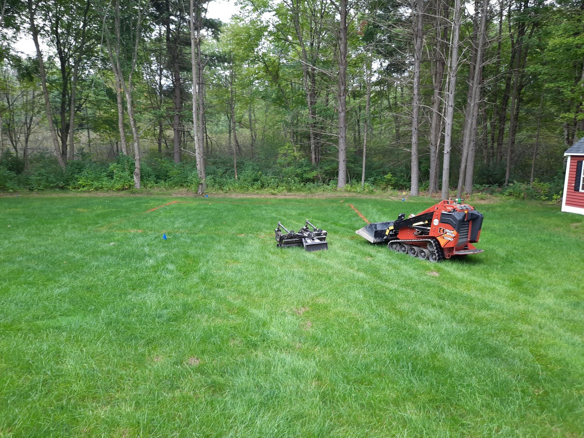 Orange lawn mower and detached attachment on a green grassy yard near trees