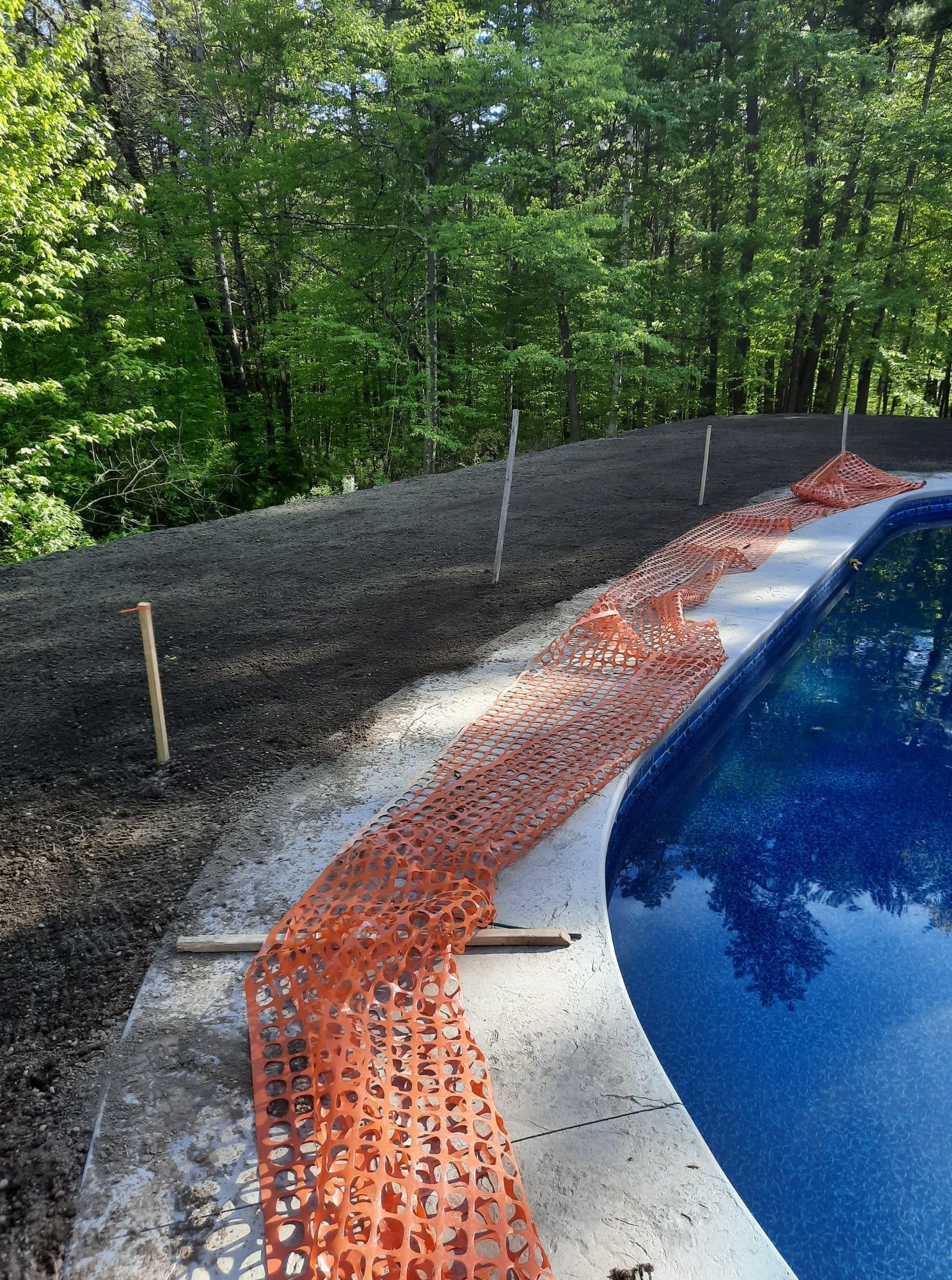 Orange erosion blanket beside a paved path and blue water, with a wooded hillside in the background