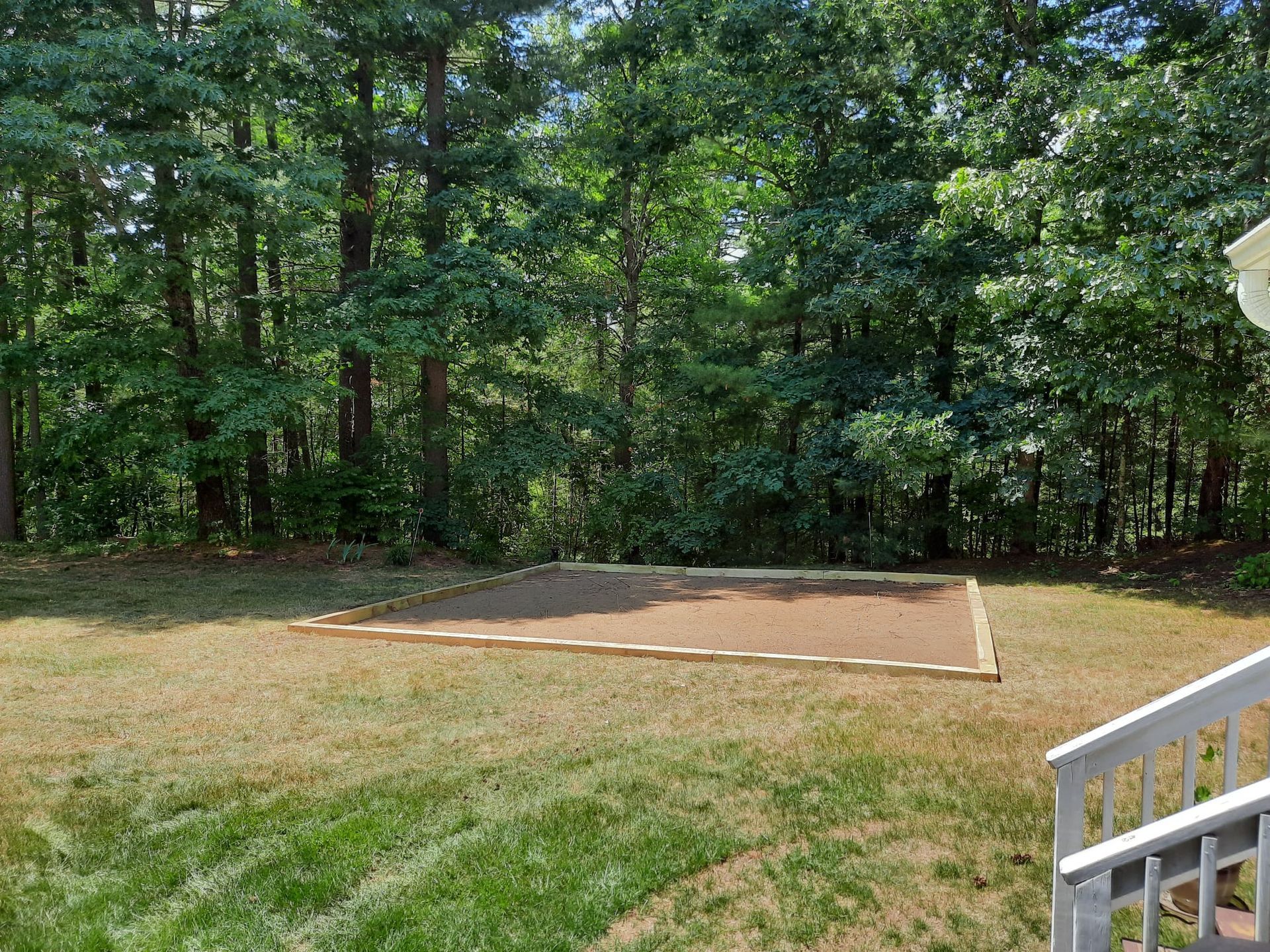 Backyard clearing with a dirt patch beside grass, trees in the background, and white railing in foreground