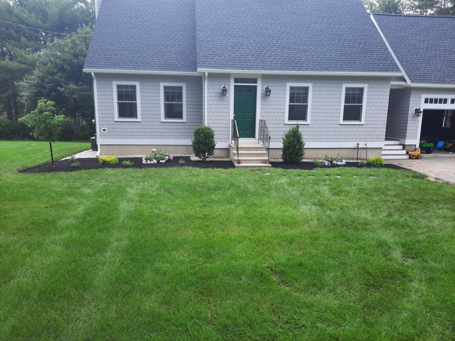 Gray house with a green front door and large lawn, viewed from the front yard.