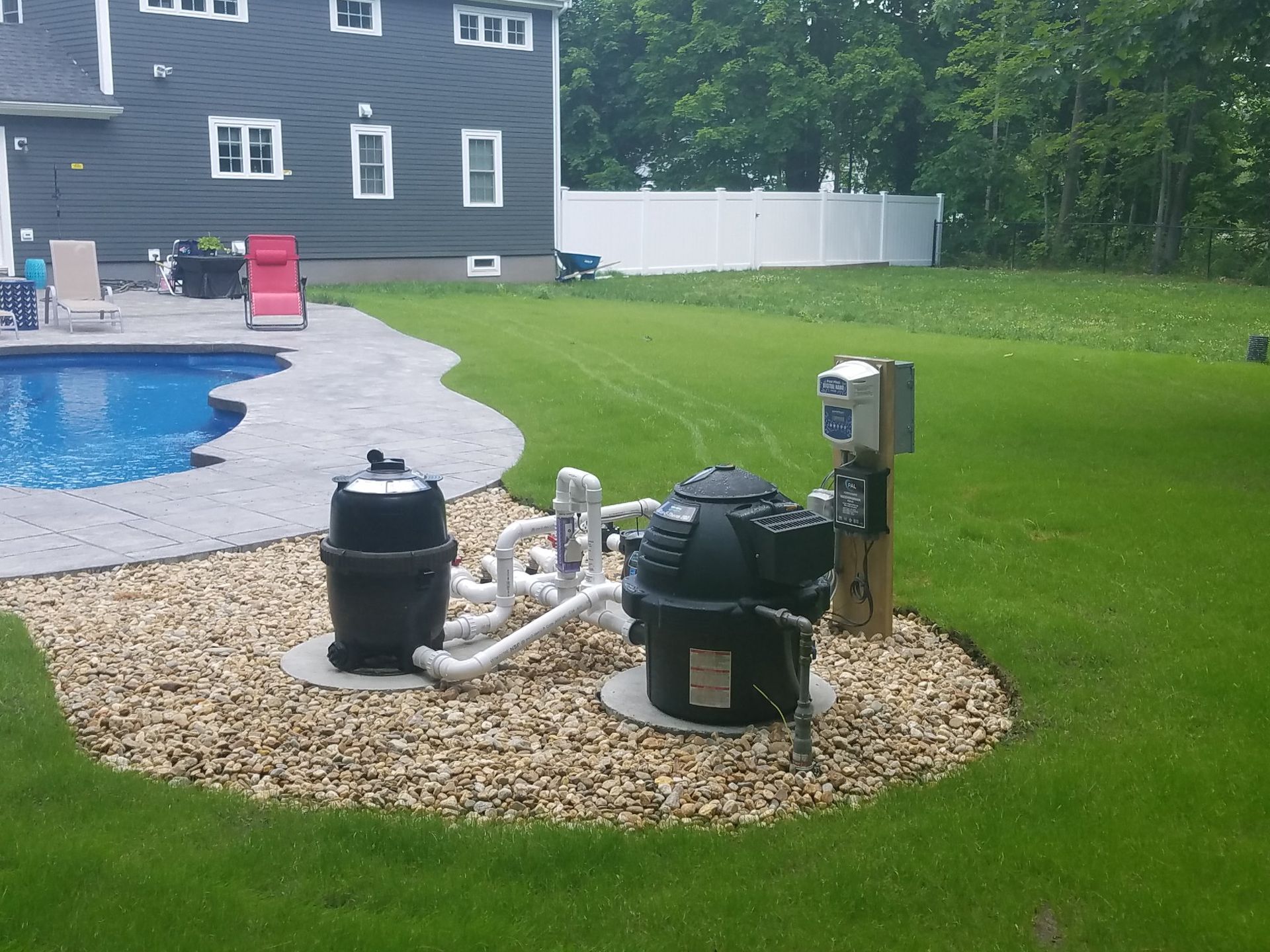 Pool equipment and pumps on gravel beside a backyard swimming pool and lawn