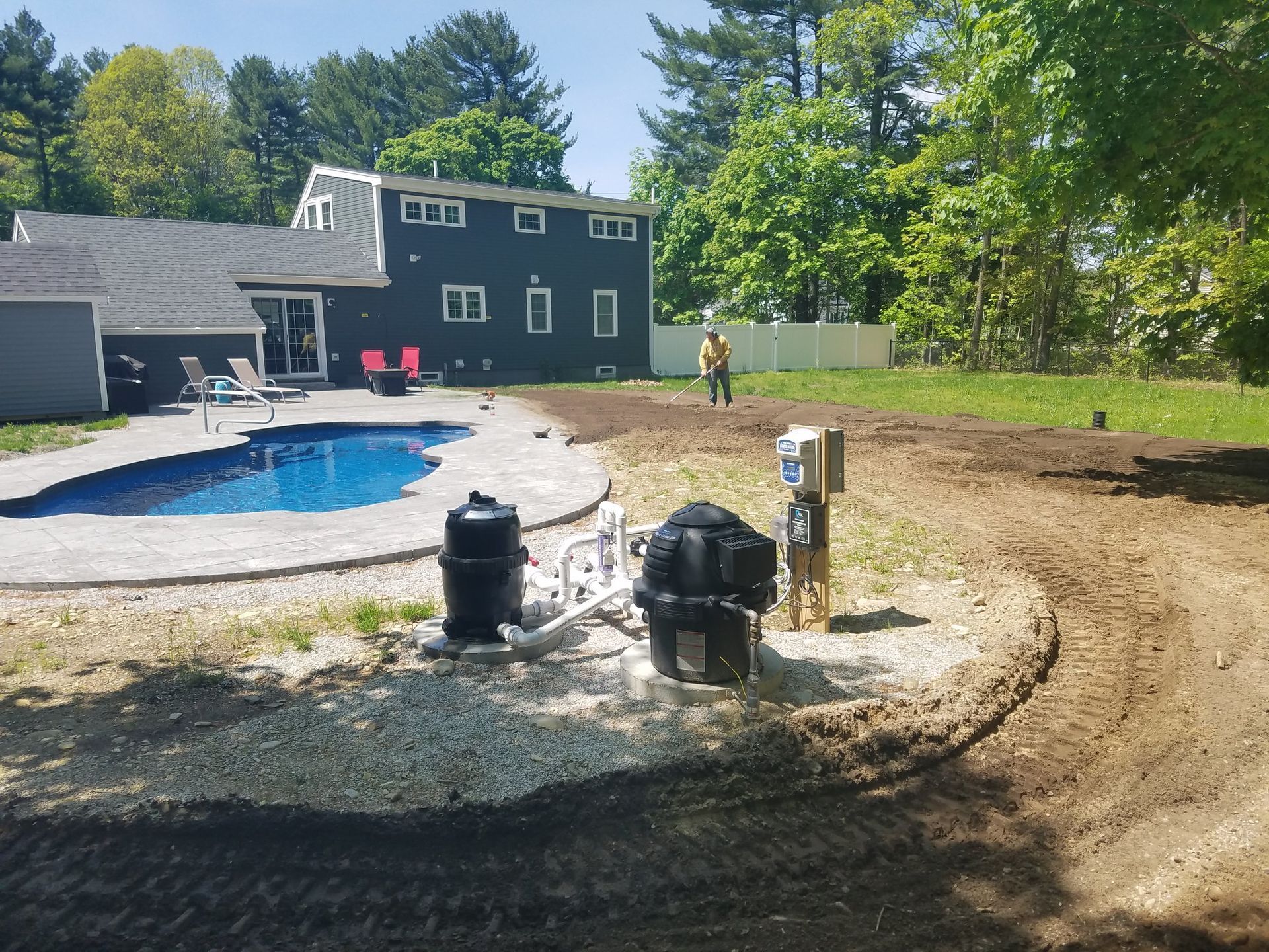 Backyard with a blue pool, dark house, gravel patio equipment, and a person near the lawn