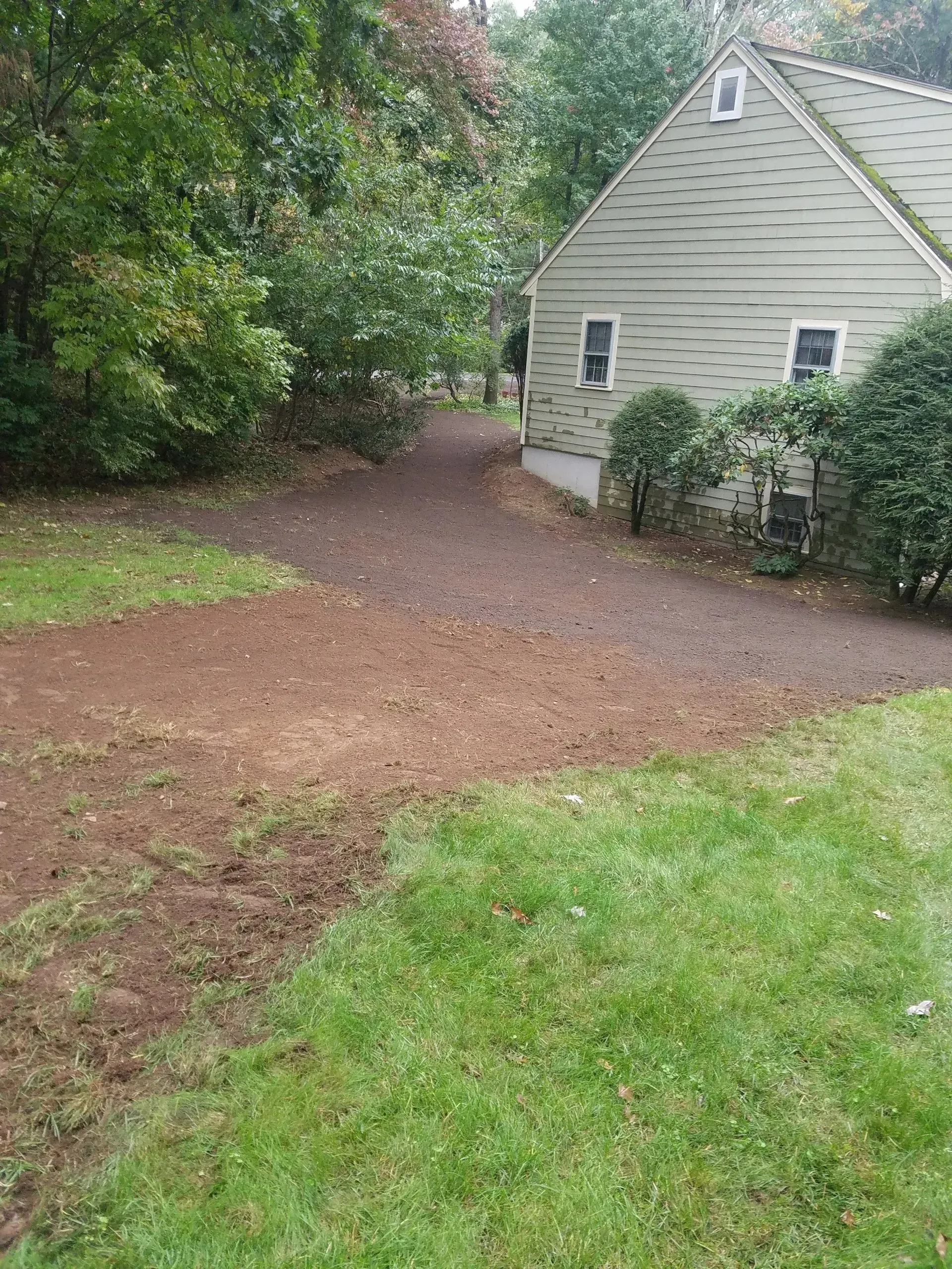 Gravel driveway beside a house, bordered by trees and green lawn.