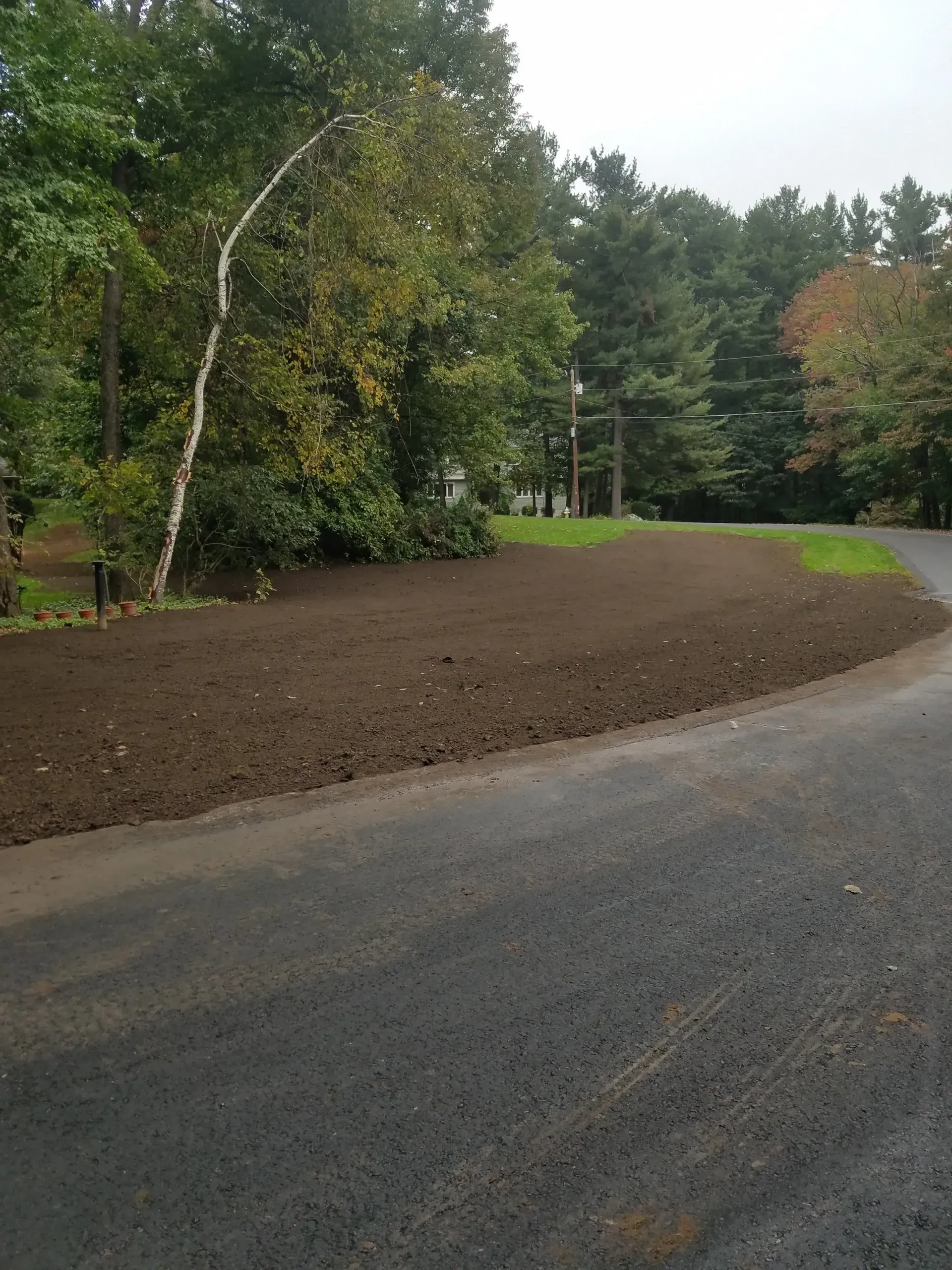 Curved gravel road beside a freshly planted soil area and trees in a wooded landscape