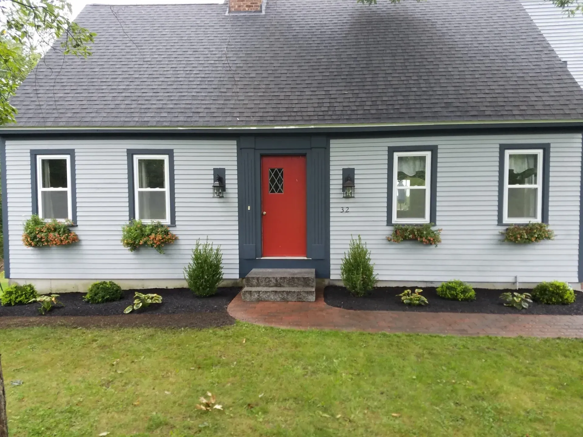 Small gray house with a red front door, white trim, flower boxes, and a green lawn.