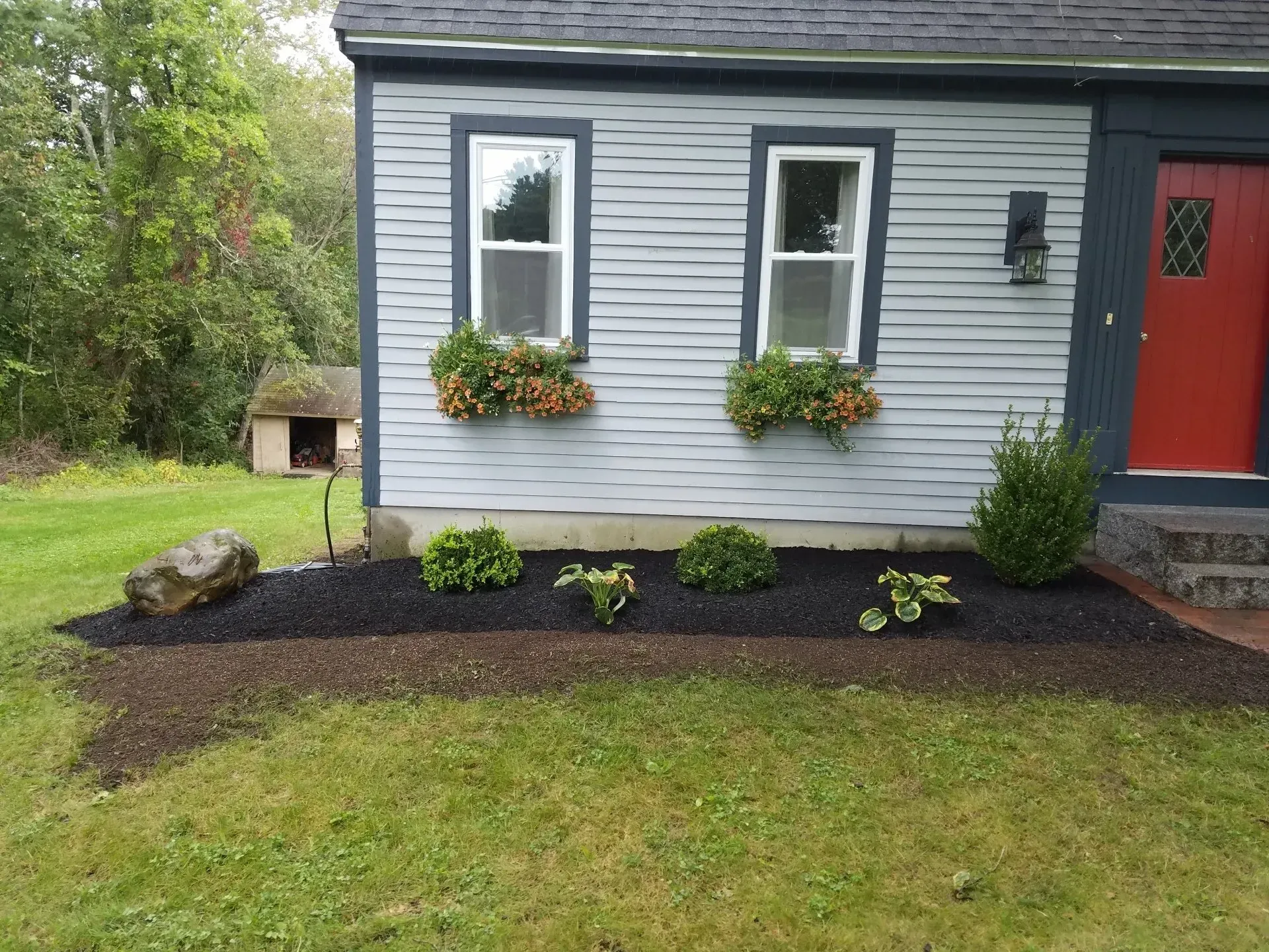 Gray house exterior with red door, two windows, and a small flower bed in front
