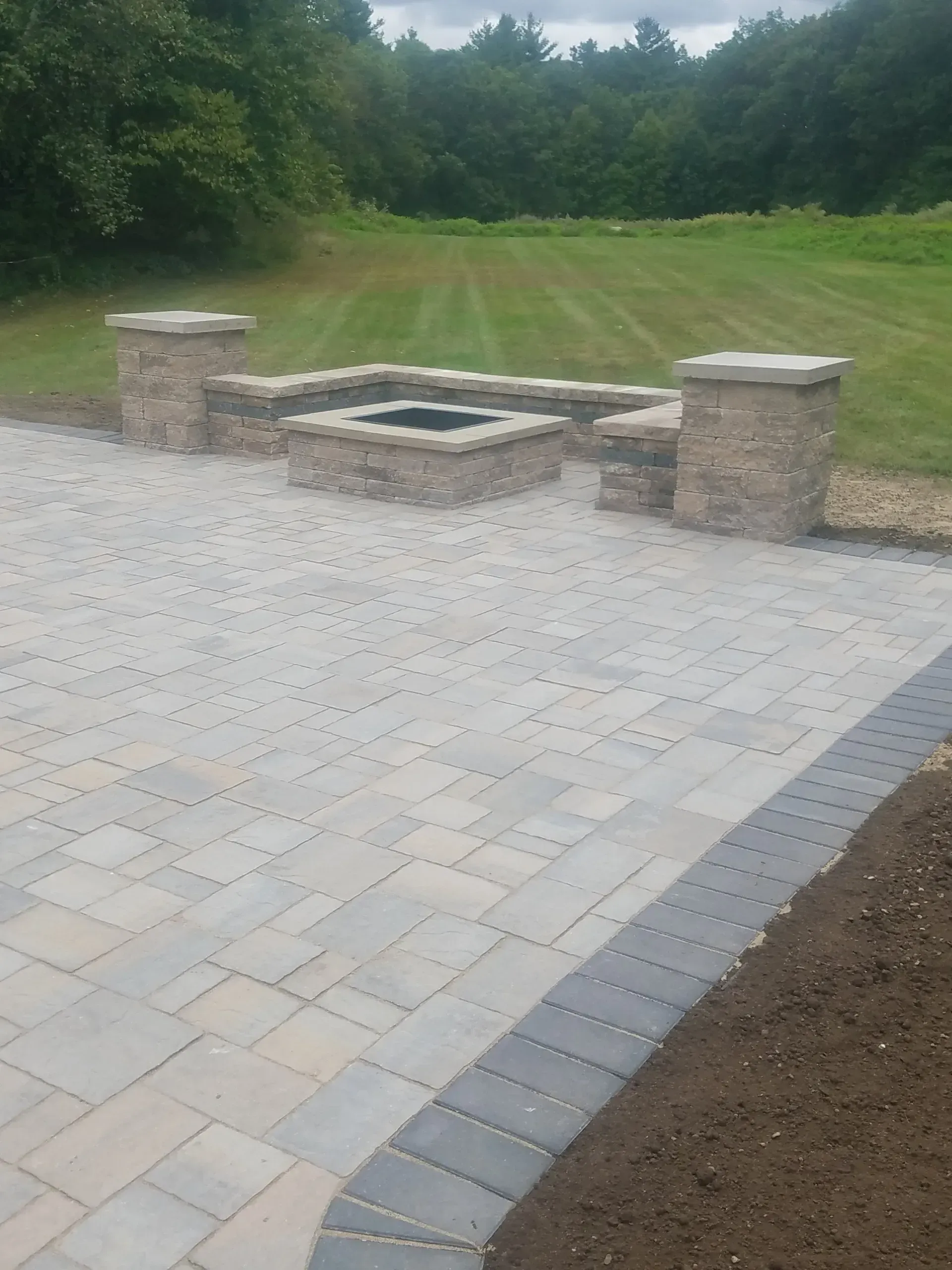 Stone patio with built-in fire pit overlooking a grassy backyard and trees
