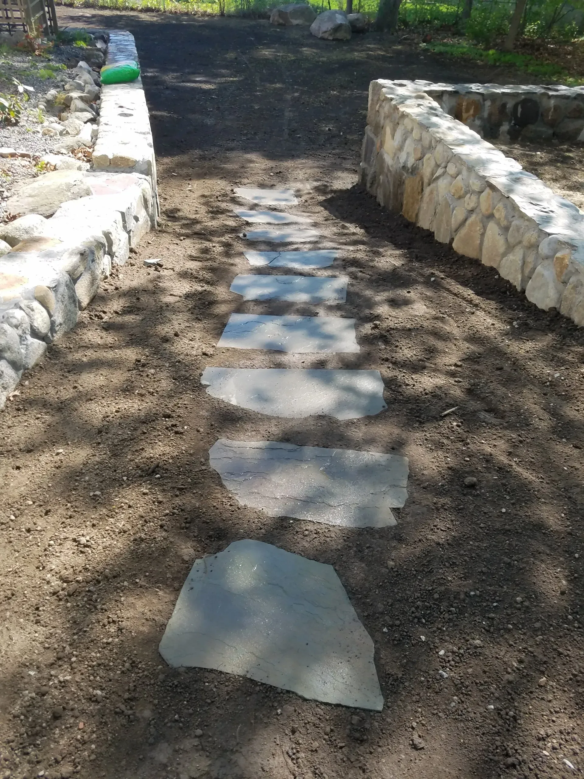 Stone stepping path through a dirt walkway bordered by low stone walls in a sunny garden