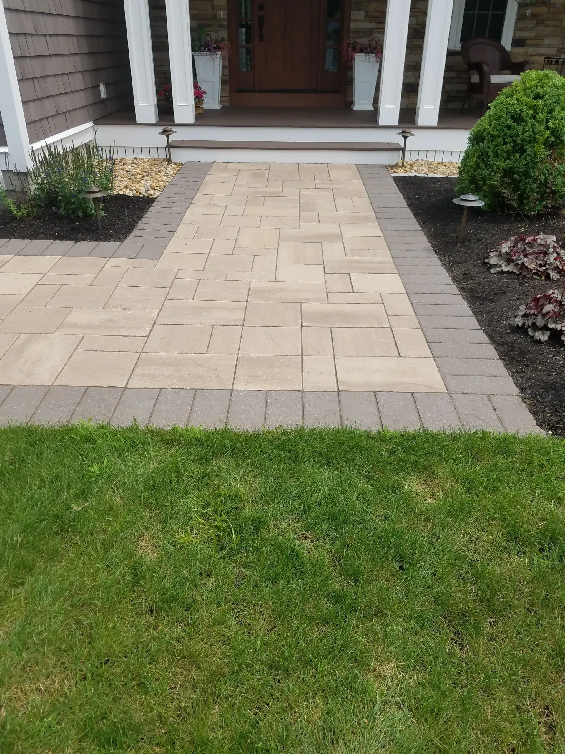Stone walkway leading to a front porch, bordered by grass and flower beds