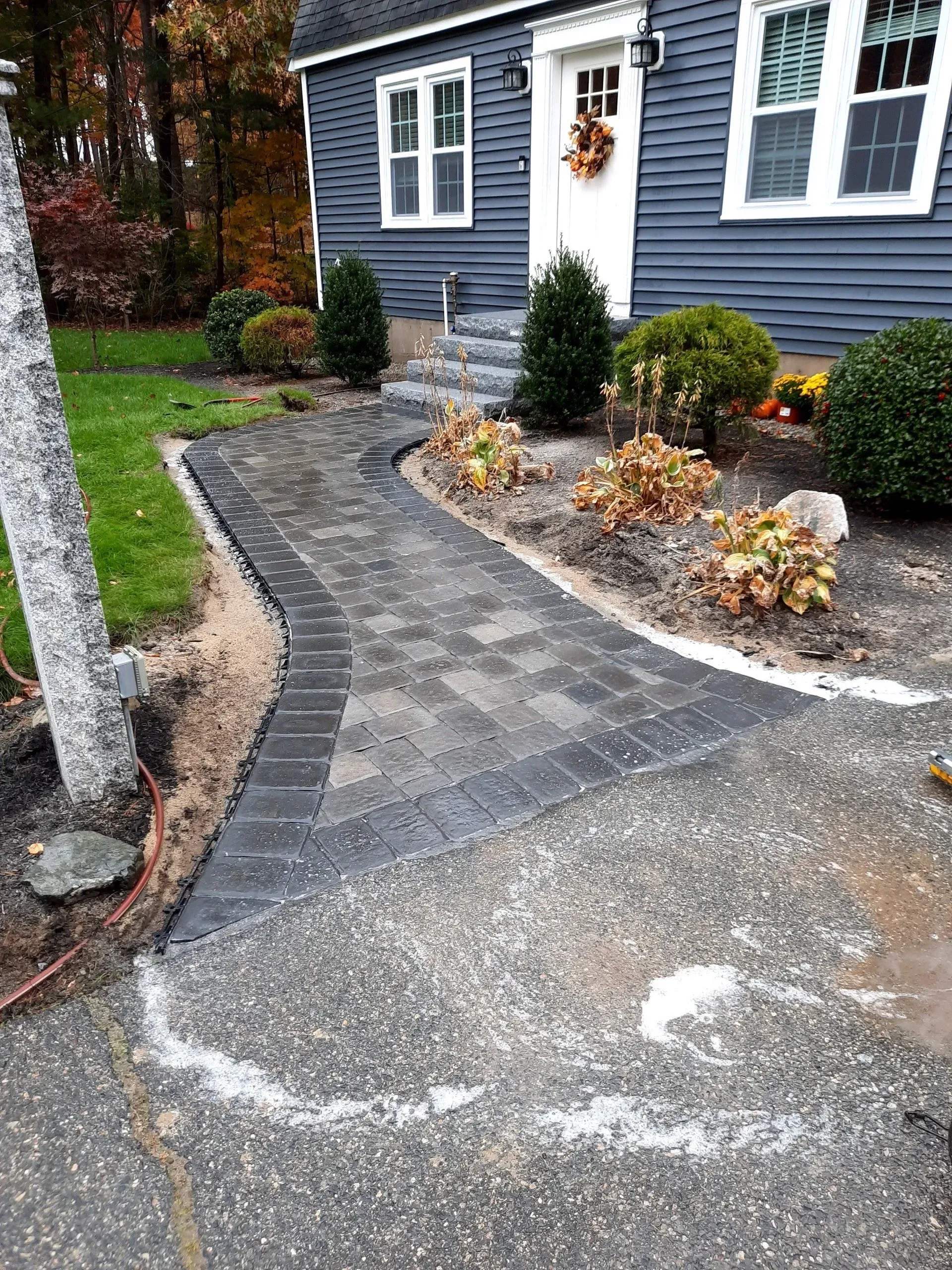 Curved gravel driveway beside a blue house with white trim and autumn landscaping