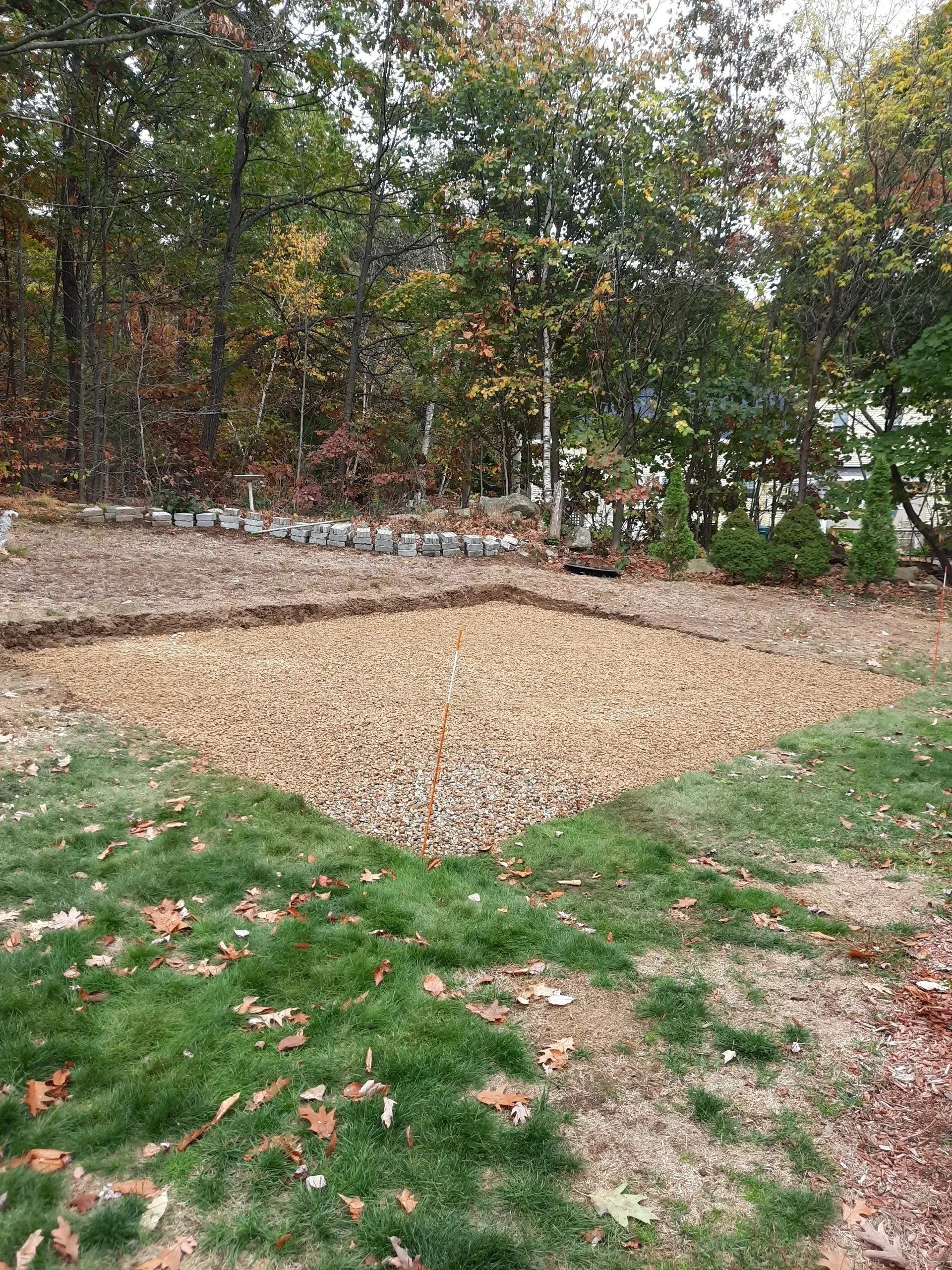 Wooded backyard with a large gravel area and a small raised garden bed covered in tan mulch.