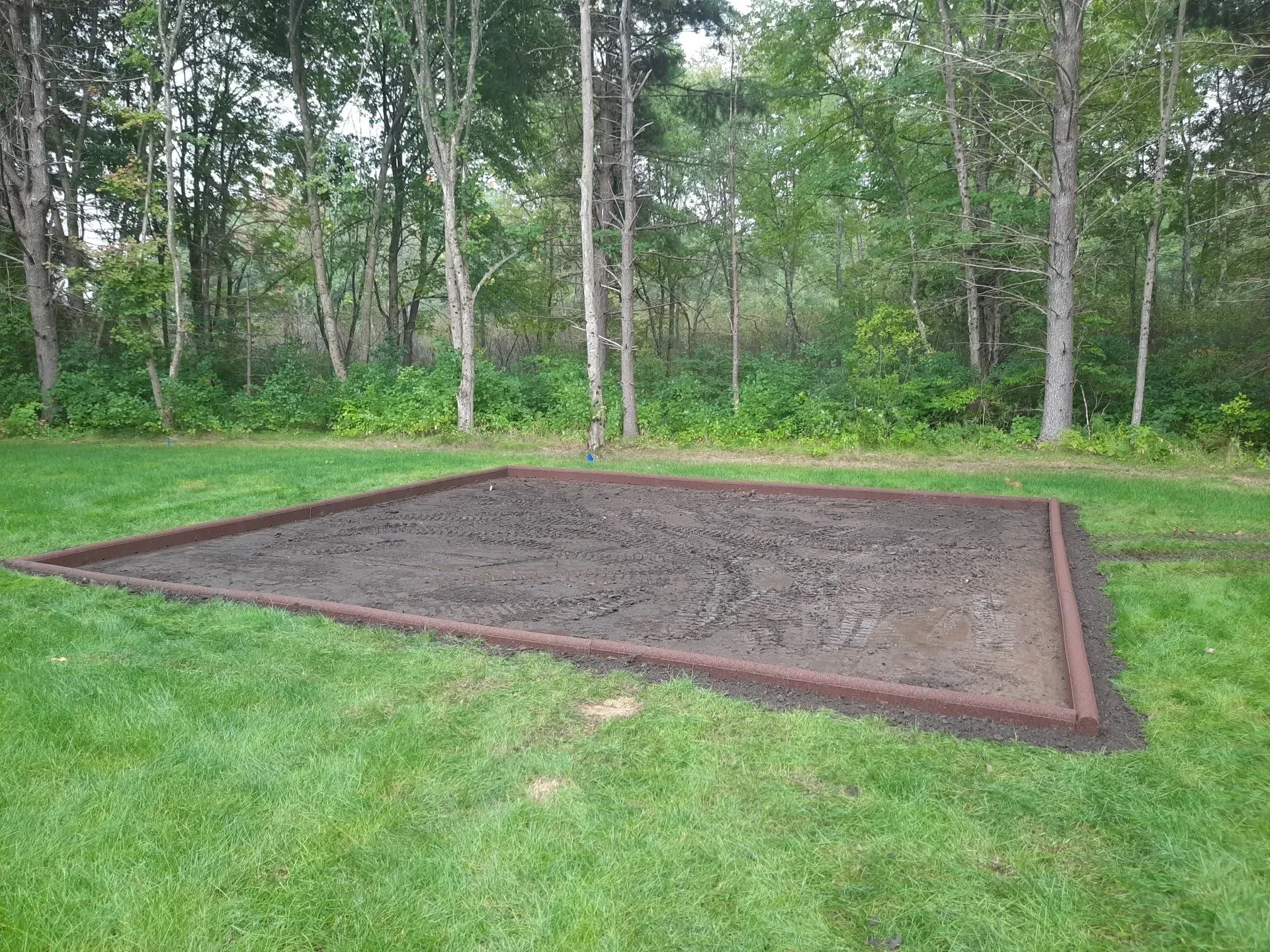 Rectangular sandbox filled with sand in a grassy yard beside a wooded area