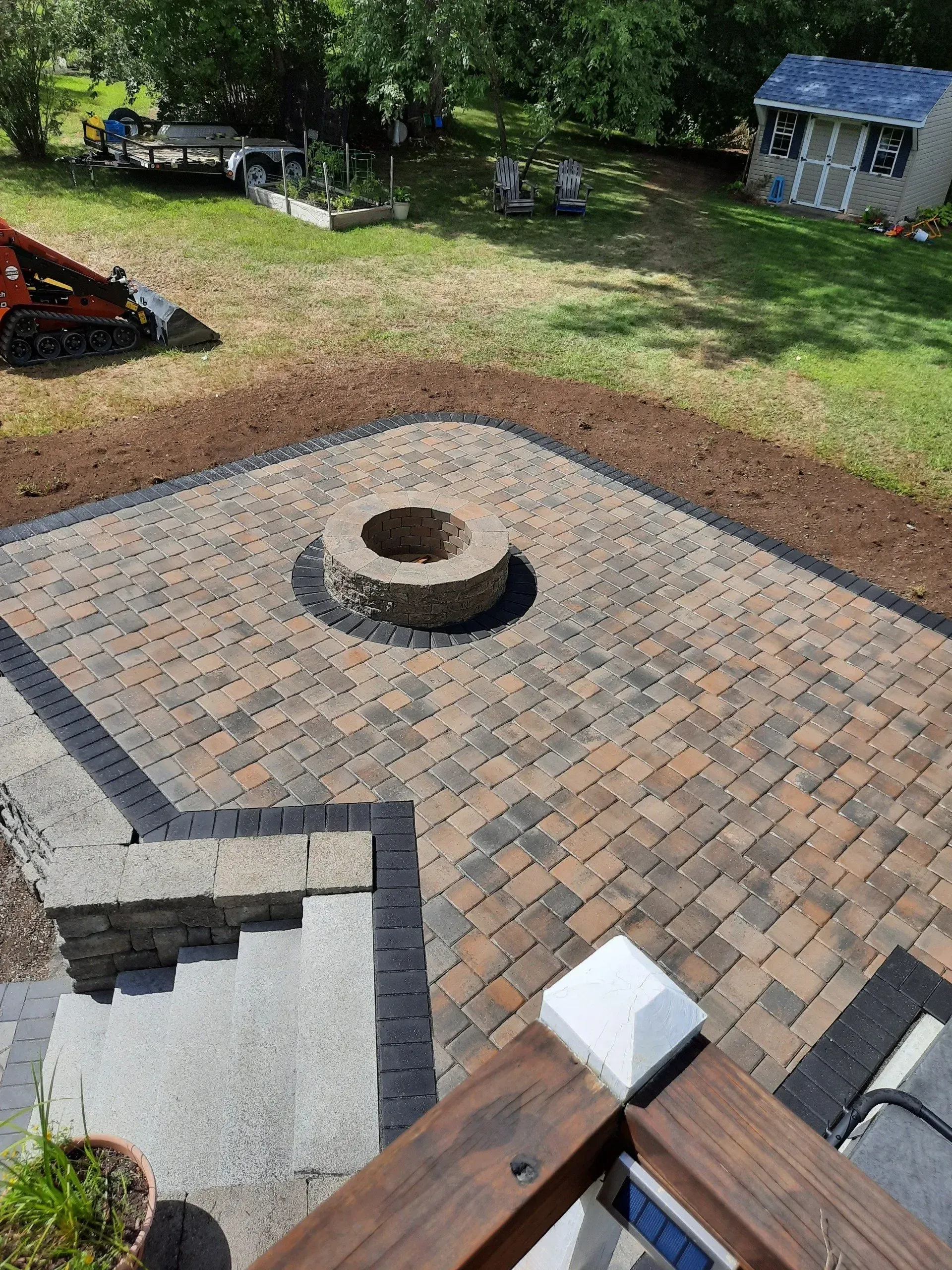 Backyard patio with paver stones, fire pit, and a small shed near trees and grass.