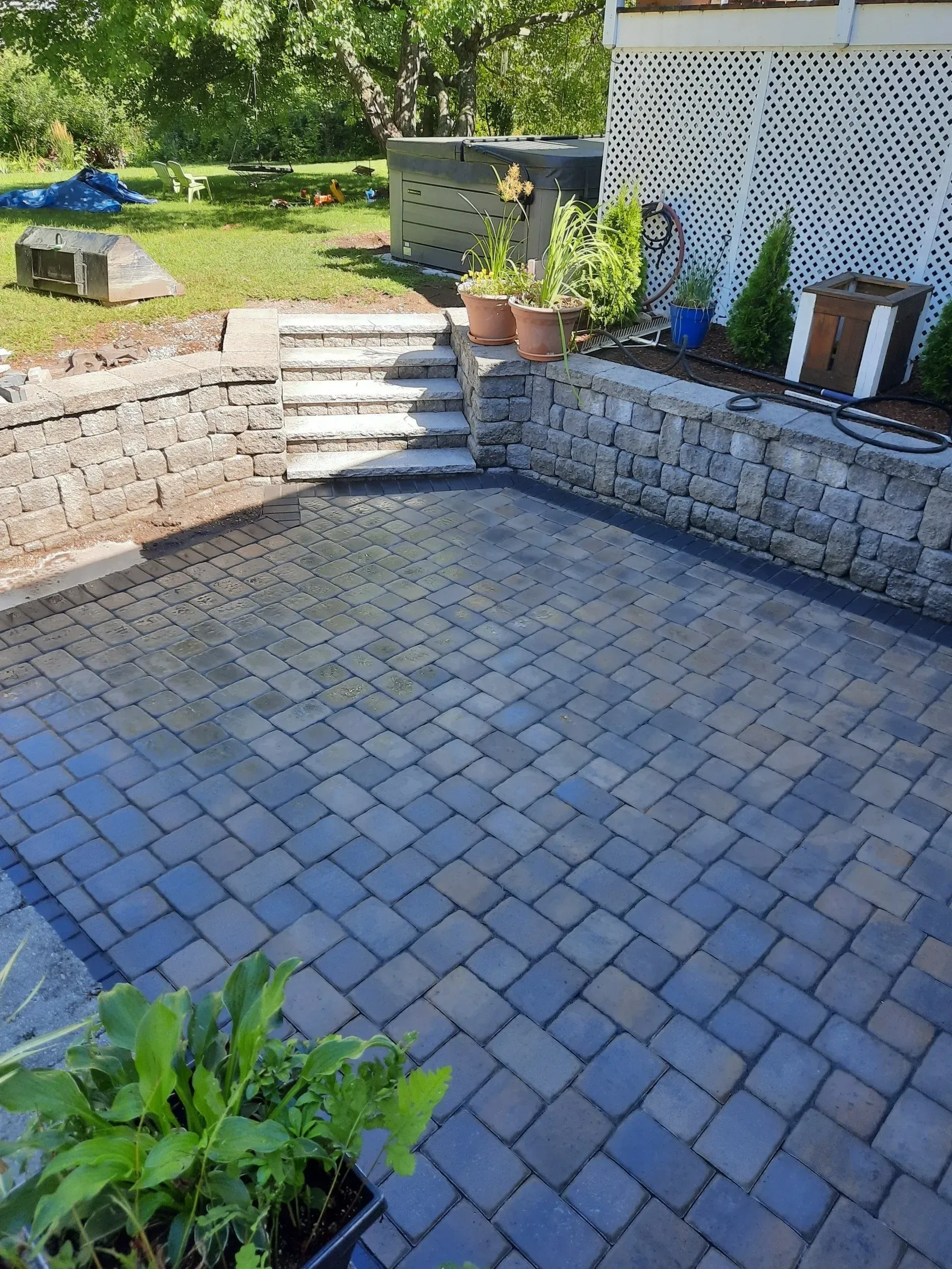 Stone patio with built-in steps, potted plants, and a lattice fence in a backyard garden.