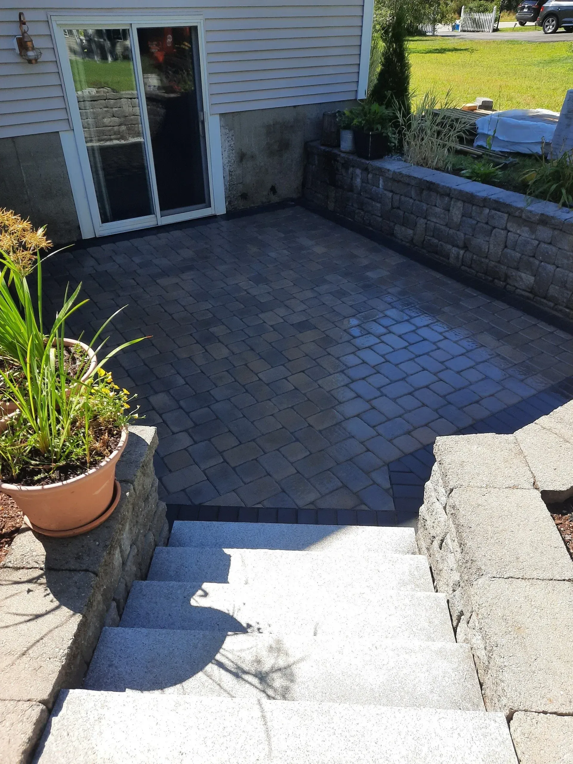 Stone patio and steps leading to a house entrance, with potted plants and raised retaining walls.