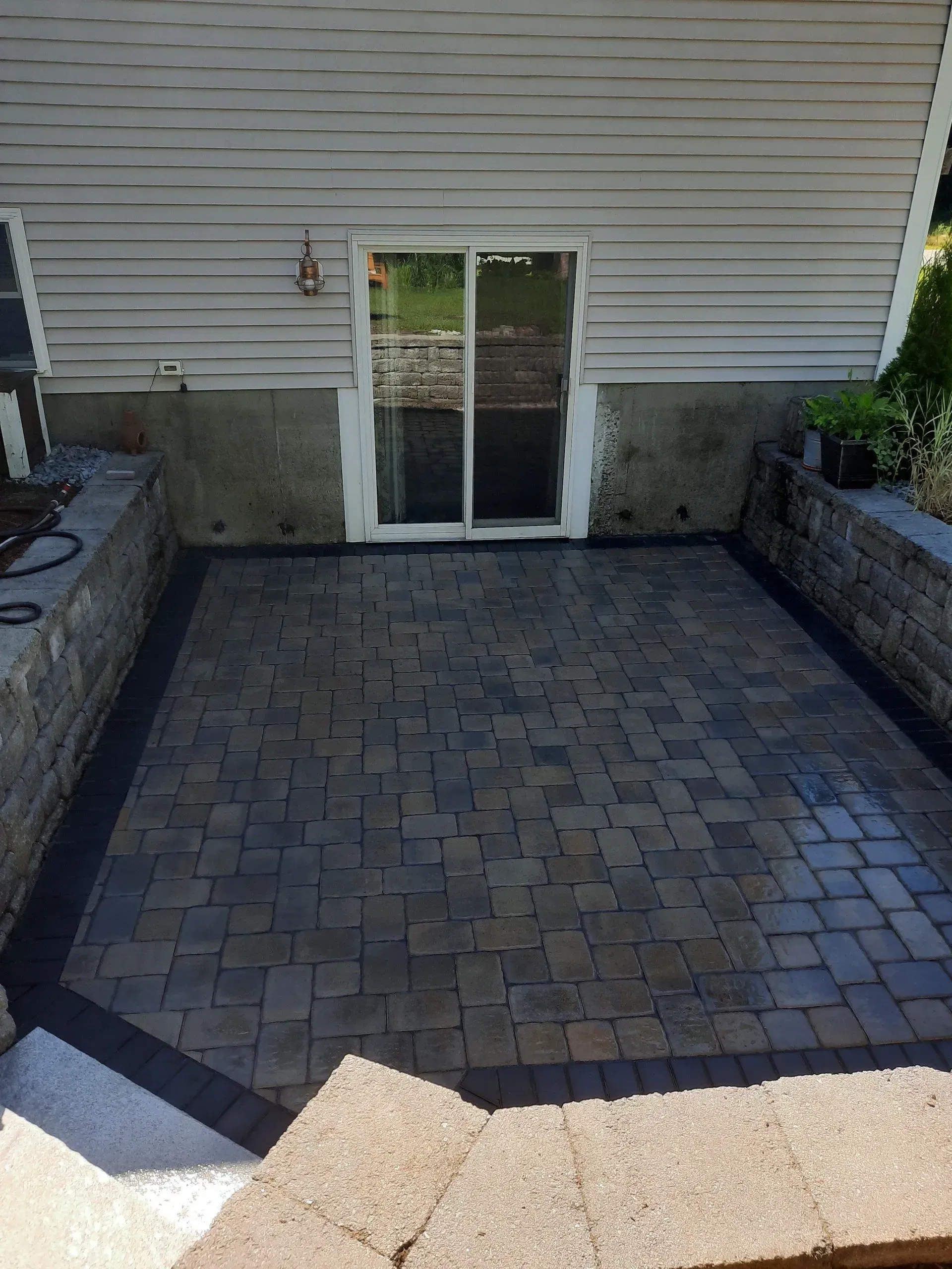 Patio with brick pavers and double glass doors beneath beige siding