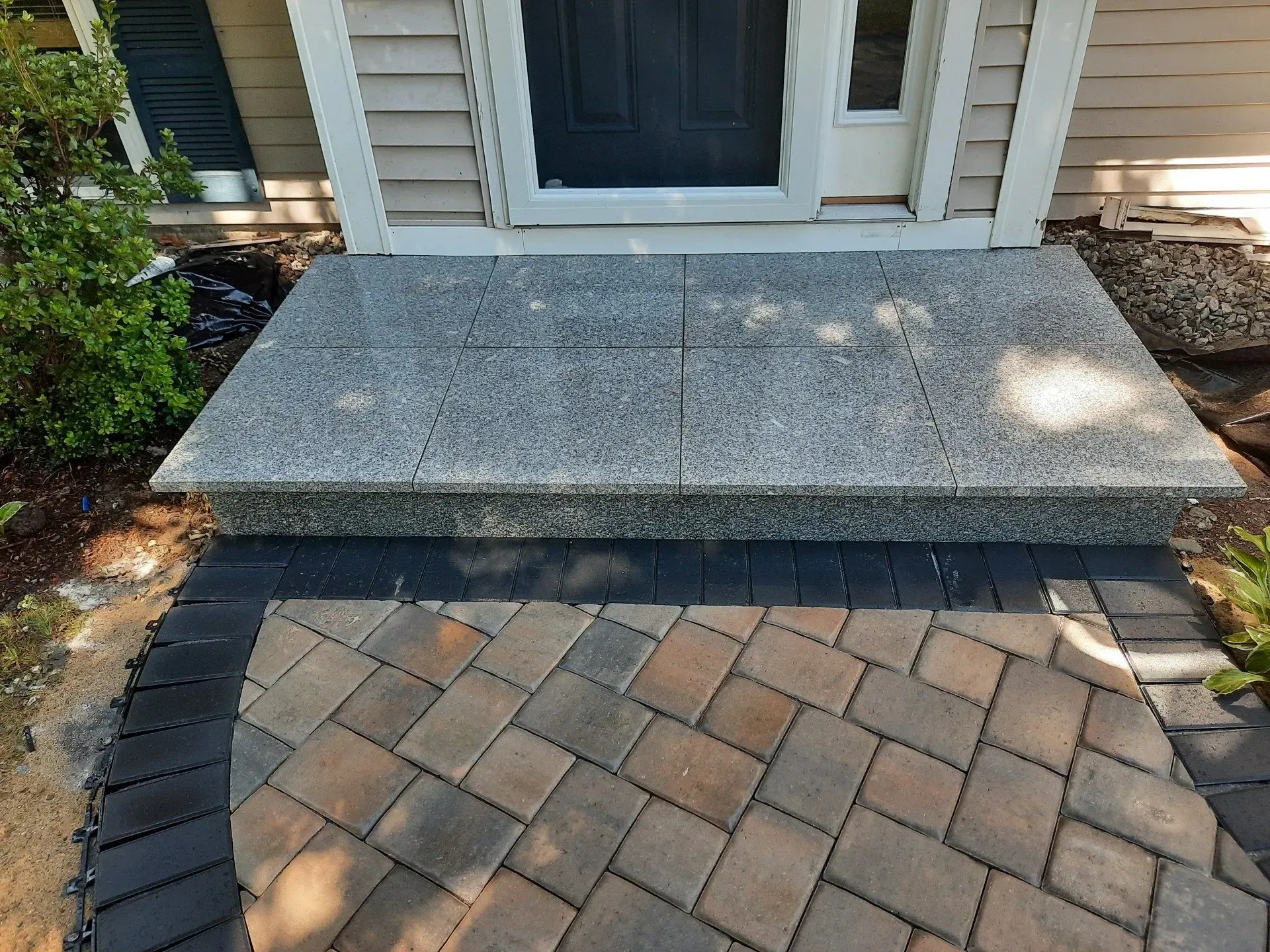 Stone front stoop and brick paver walkway leading to a house entrance