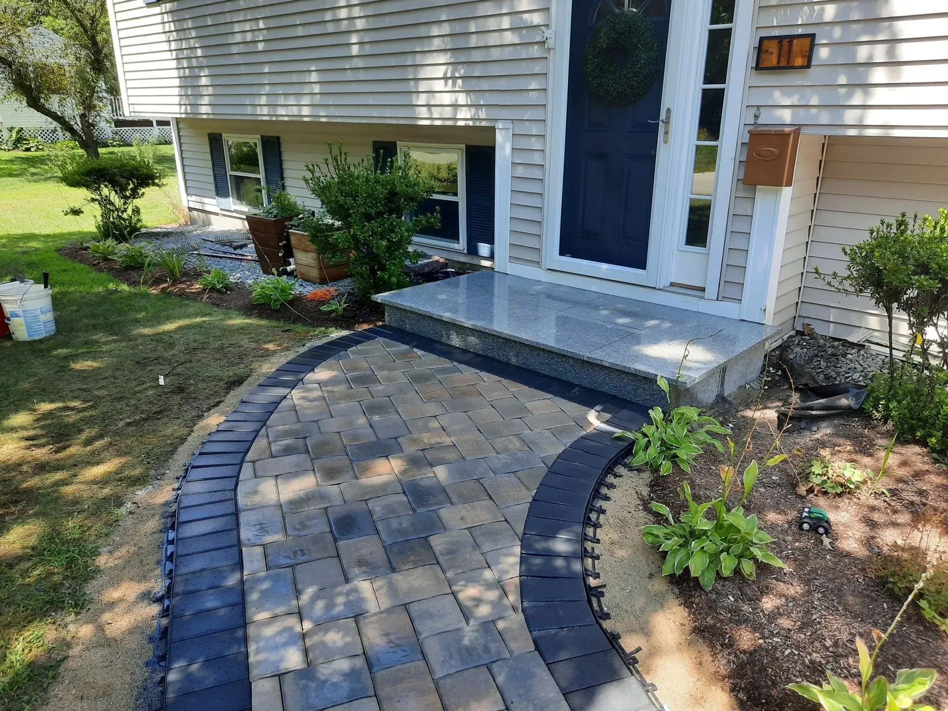 Curved brick walkway leading to a house entry with black border and landscaped garden beds