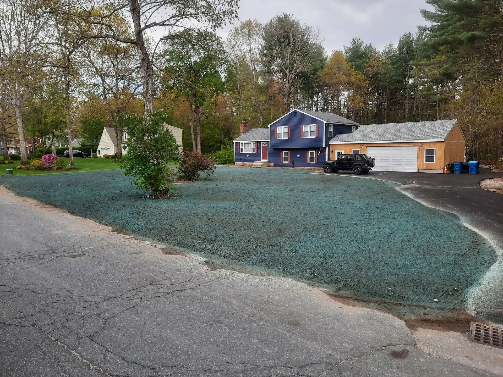 Blue house with white garage beside a large blue gravel yard on a quiet tree-lined street