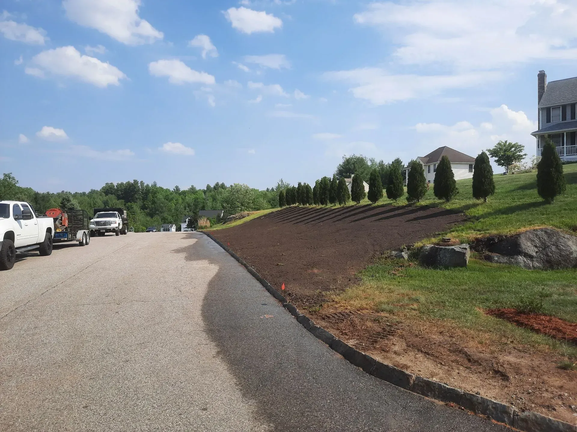 Gravel driveway curving past parked cars and a landscaped lawn beside a large house under a blue sky