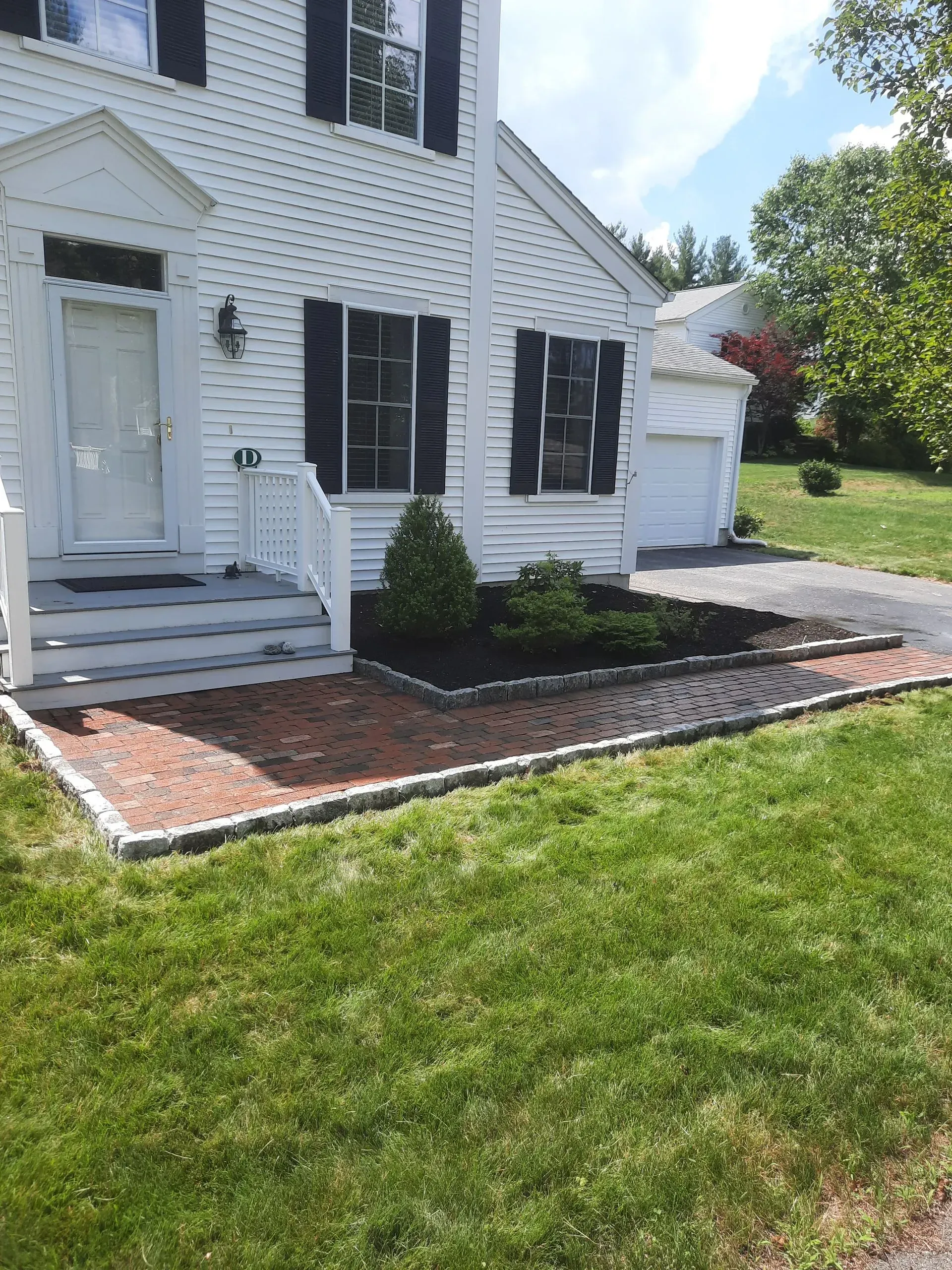 White house exterior with black shutters, small front steps, and a landscaped yard with a detached garage.