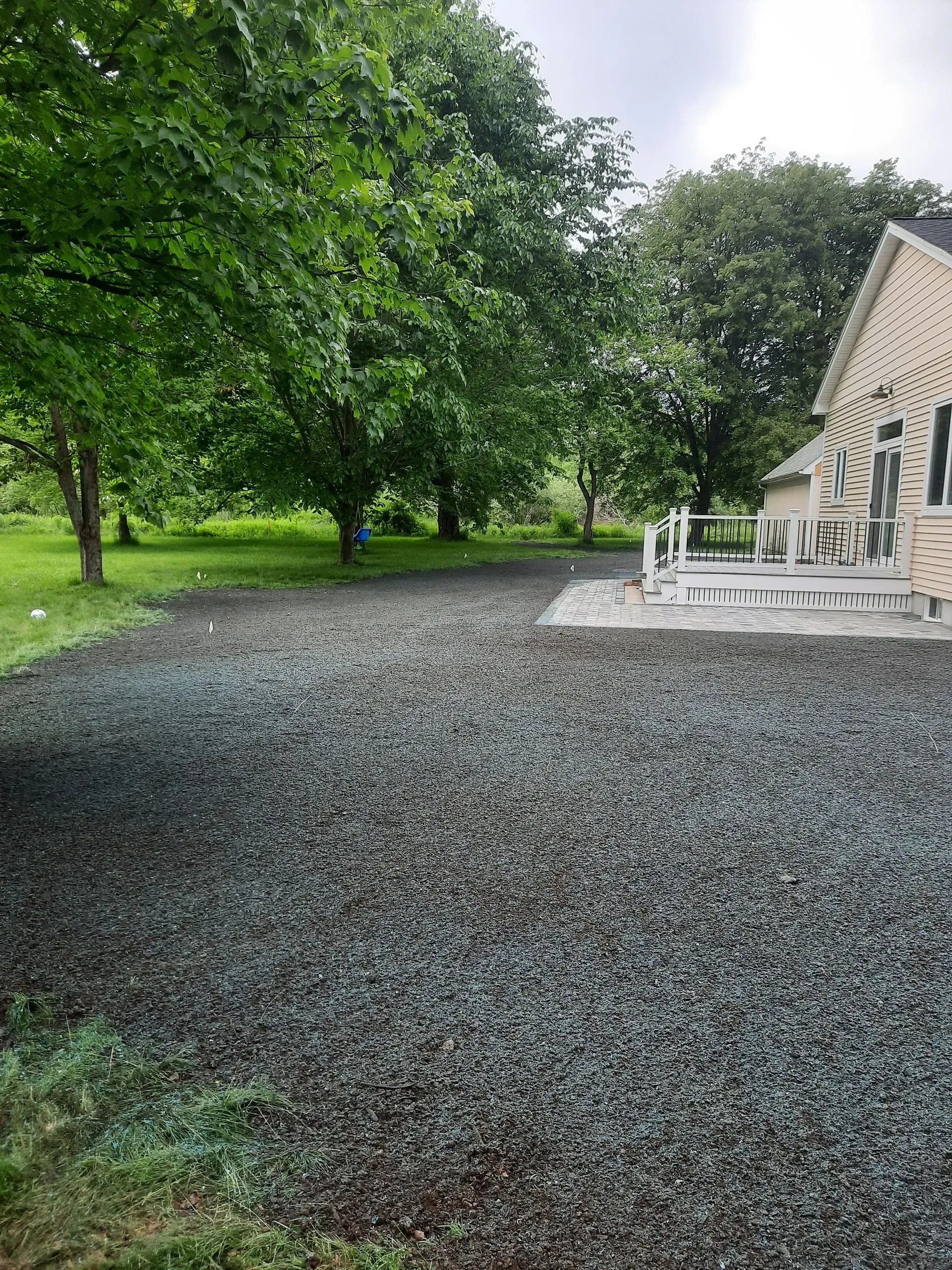 Stone gravel yard beside a stone house with white porch chairs, bordered by green trees and lawn.