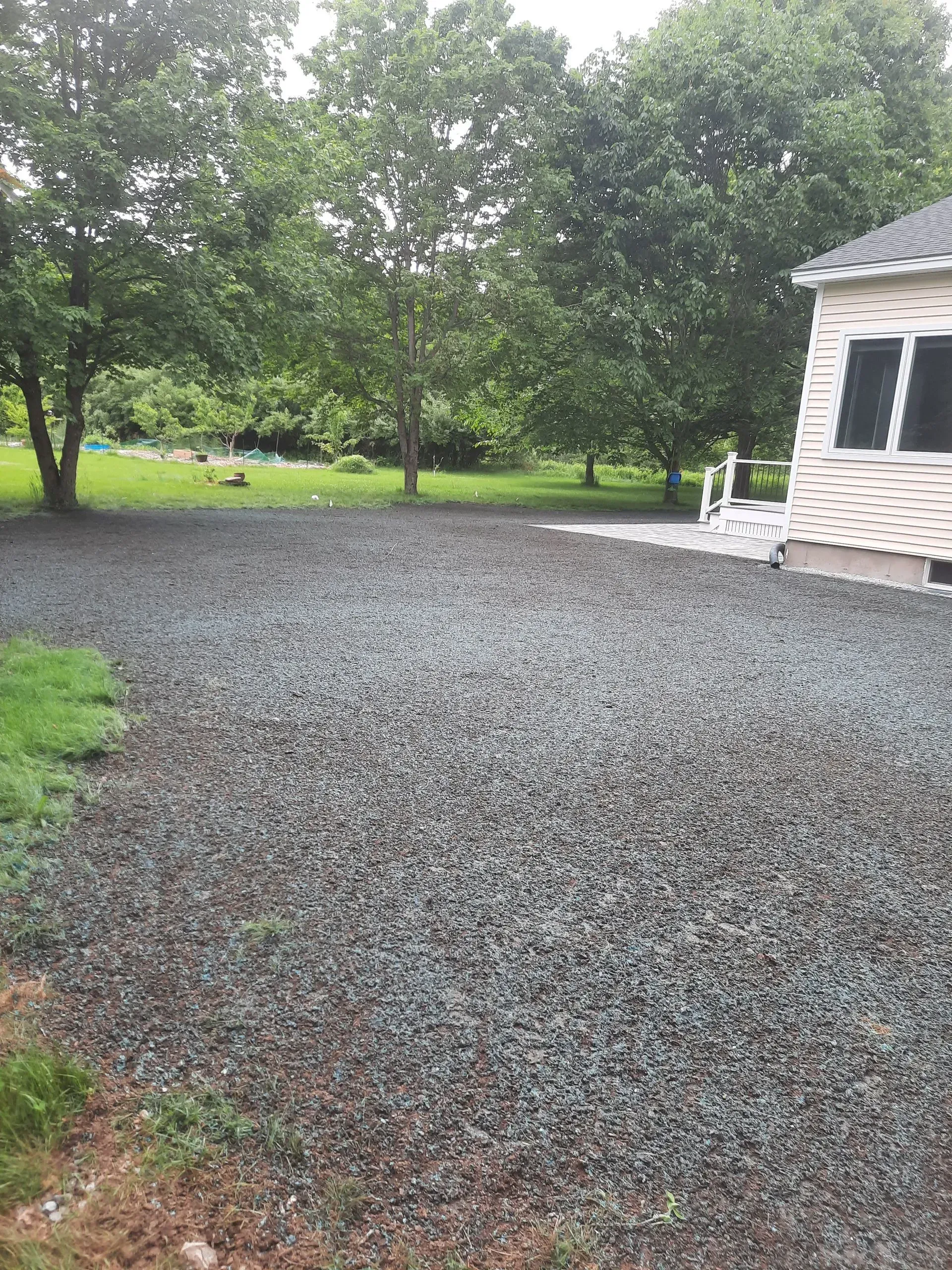Gravel driveway beside a house, with trees and green lawn in the background.
