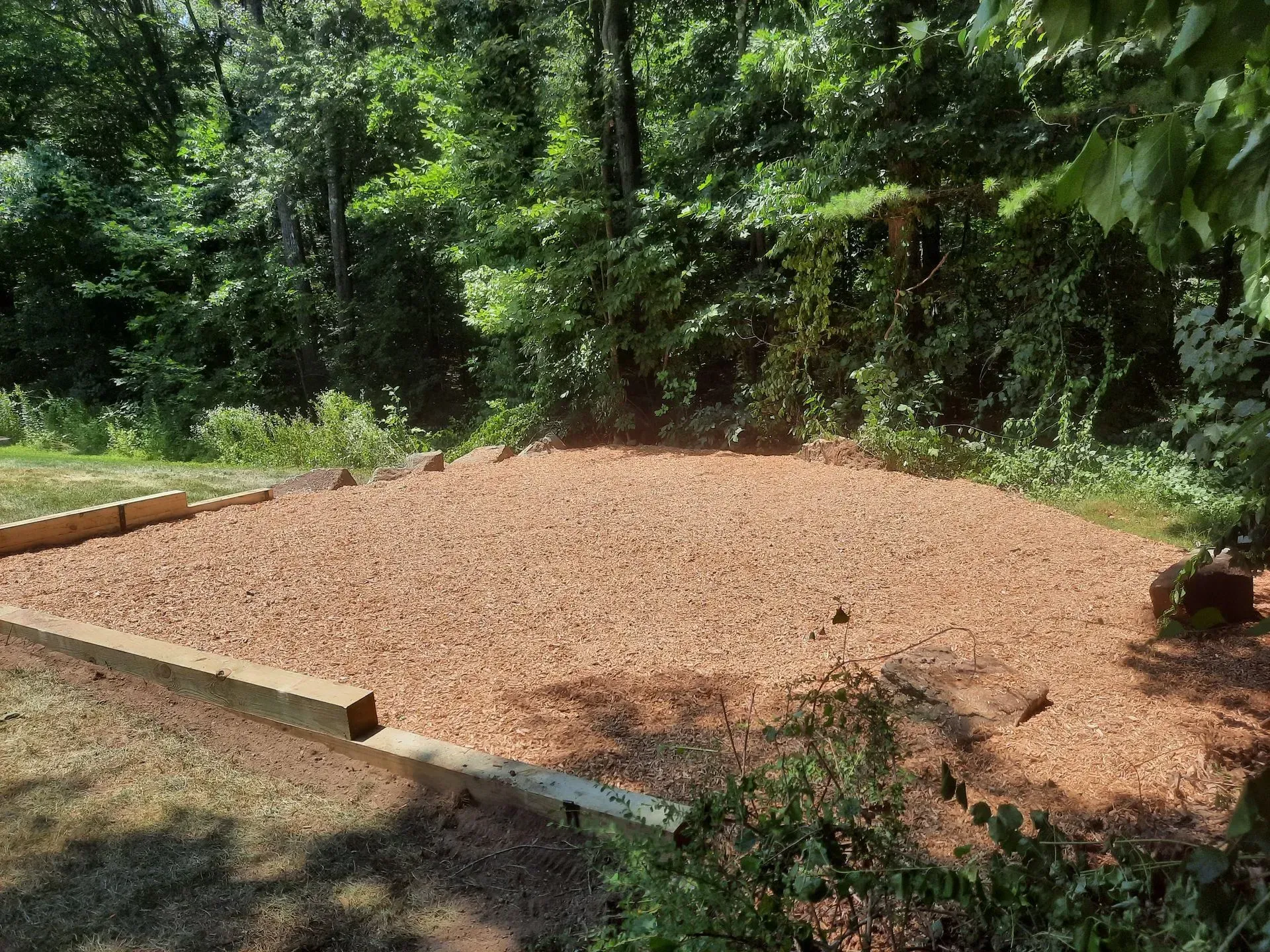 Freshly leveled brown gravel pad bordered by timber in a wooded area