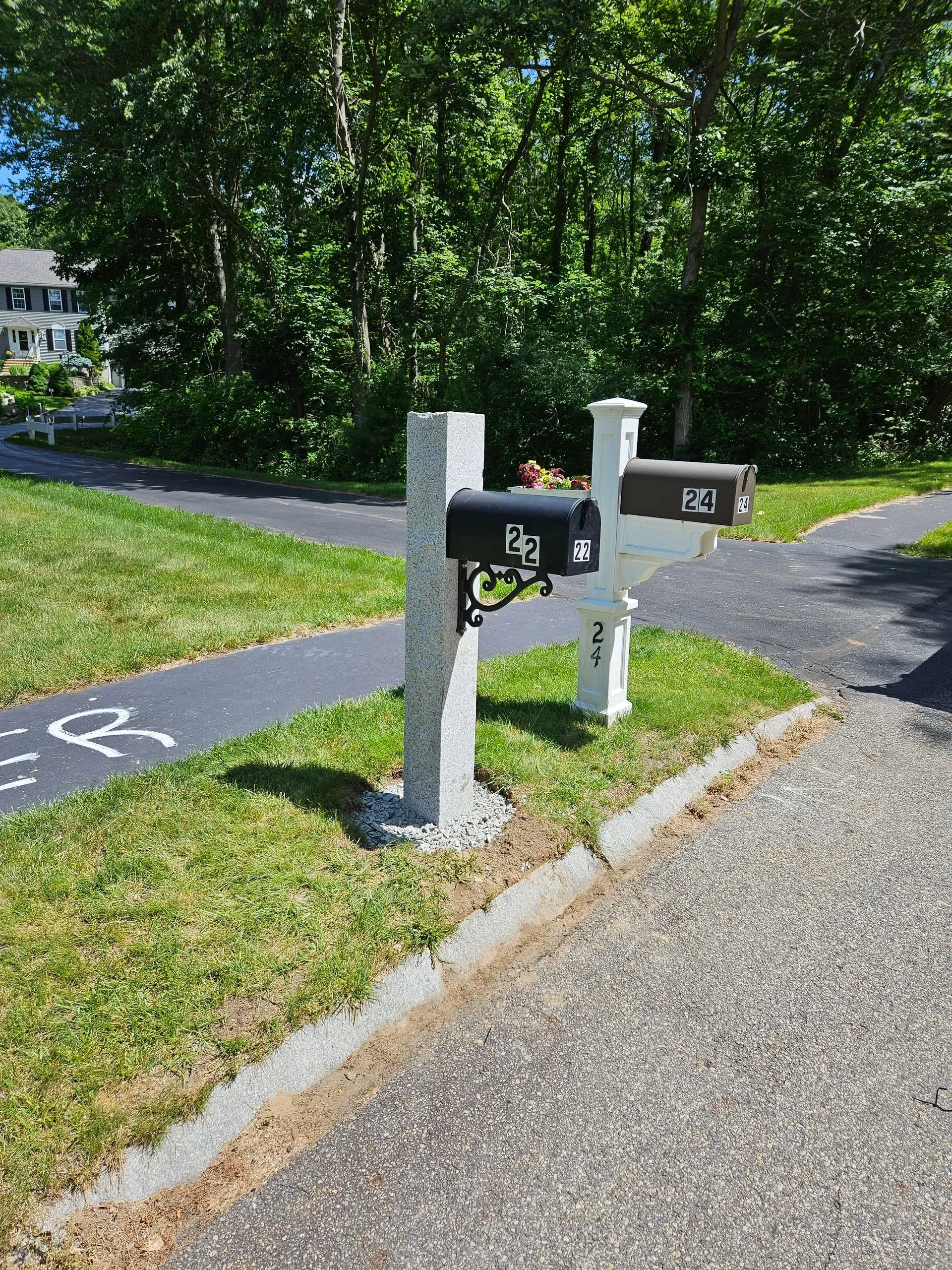 Two black mailboxes on posts beside a gravel driveway and green lawn on a sunny day