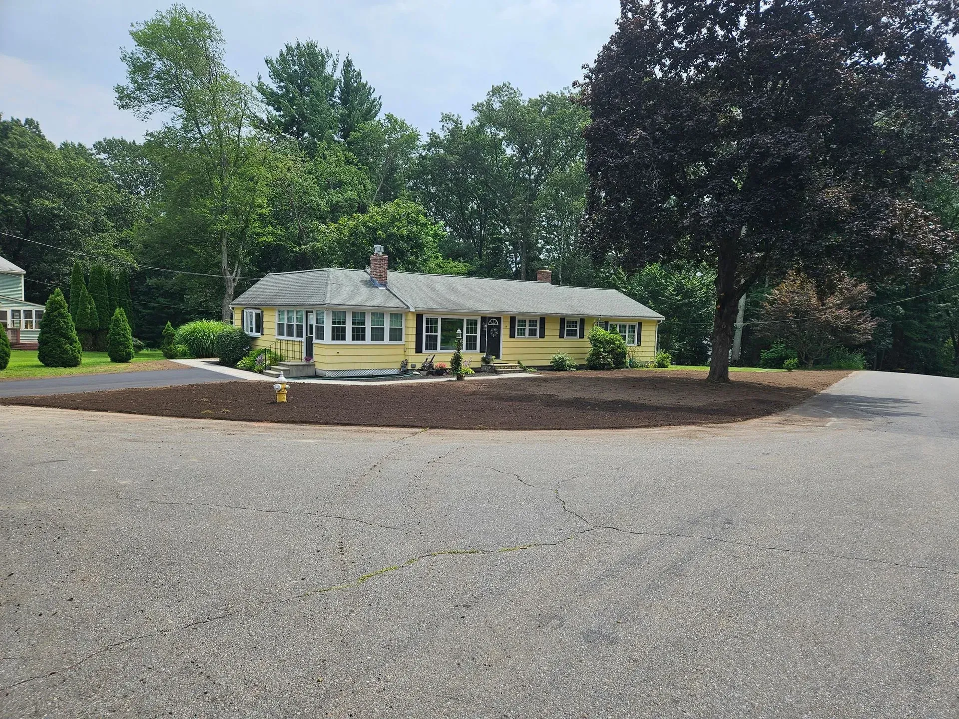 Single-story yellow house with a large gravel driveway and trees in front