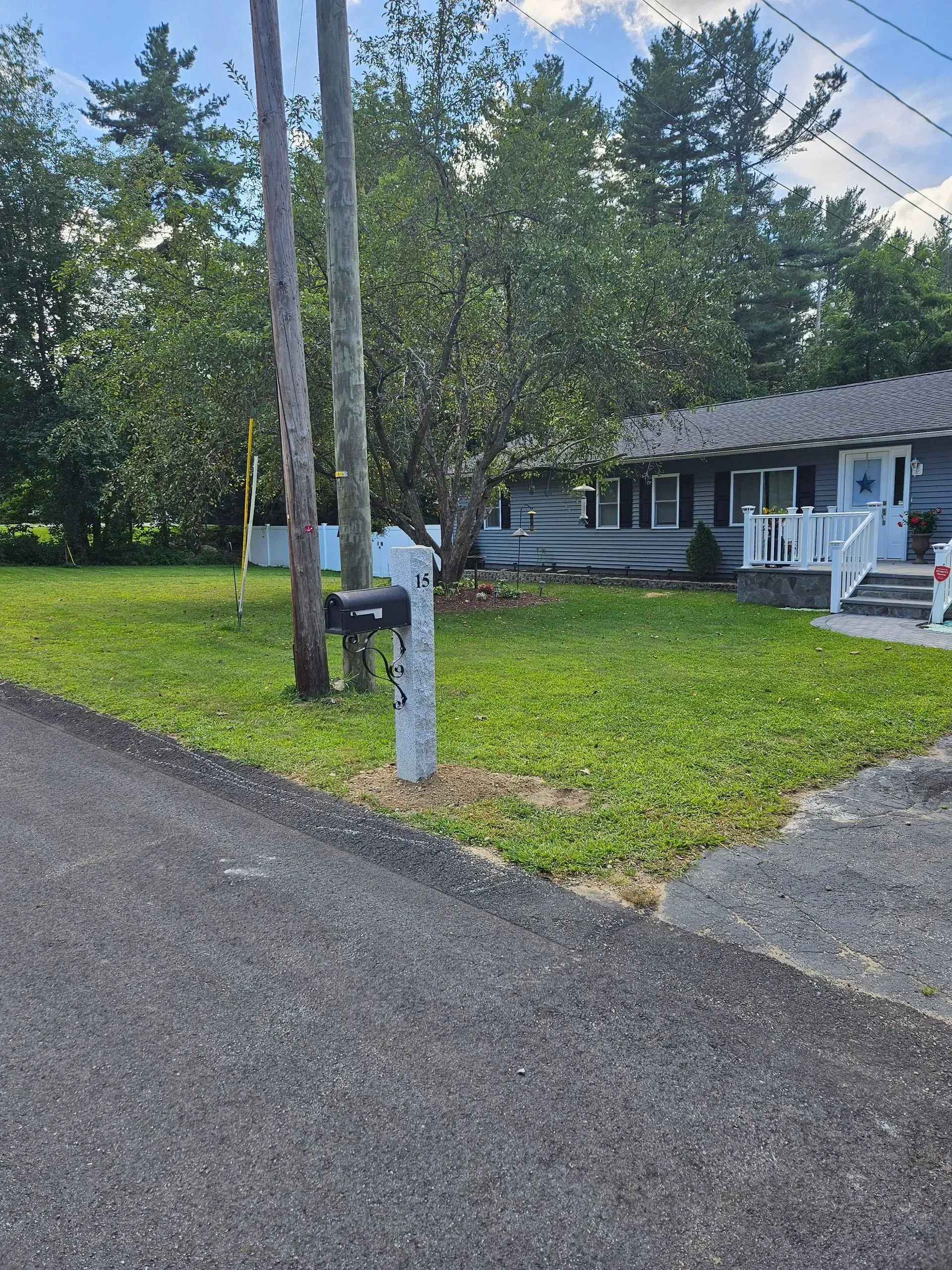 Rural cabin with porch chairs, gravel driveway, and grassy yard under trees on a sunny day