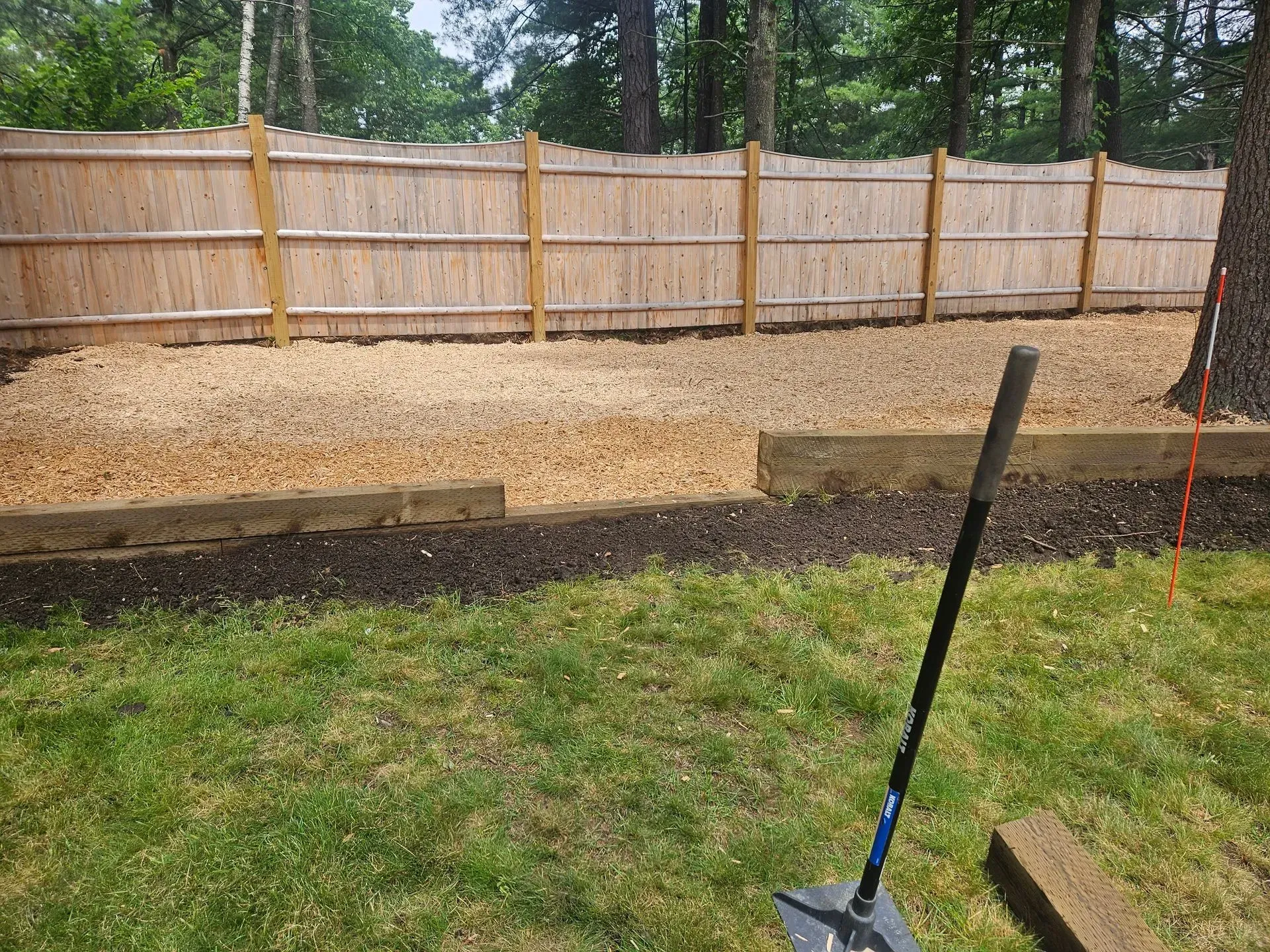 Backyard with a new raised garden bed, fresh soil, and a wooden privacy fence under trees