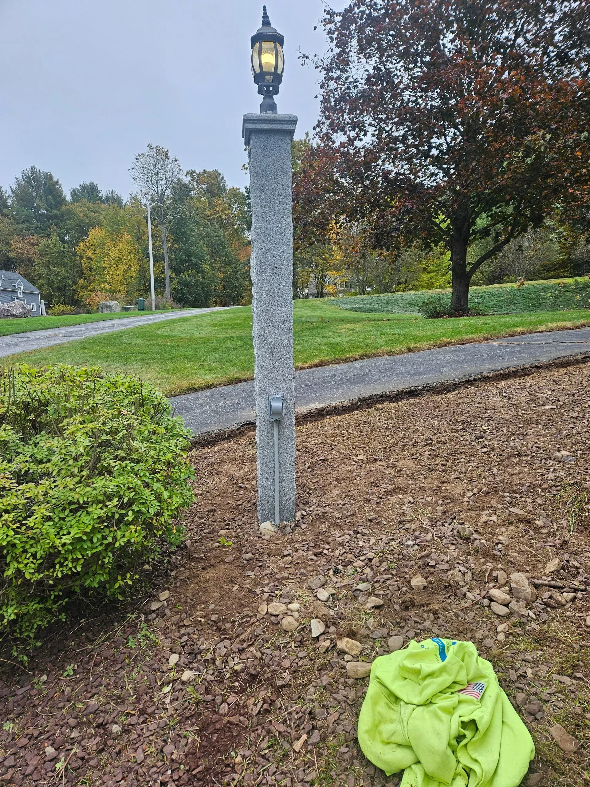 Stone lamp post in a landscaped yard with autumn trees and a bright green cloth on the mulch
