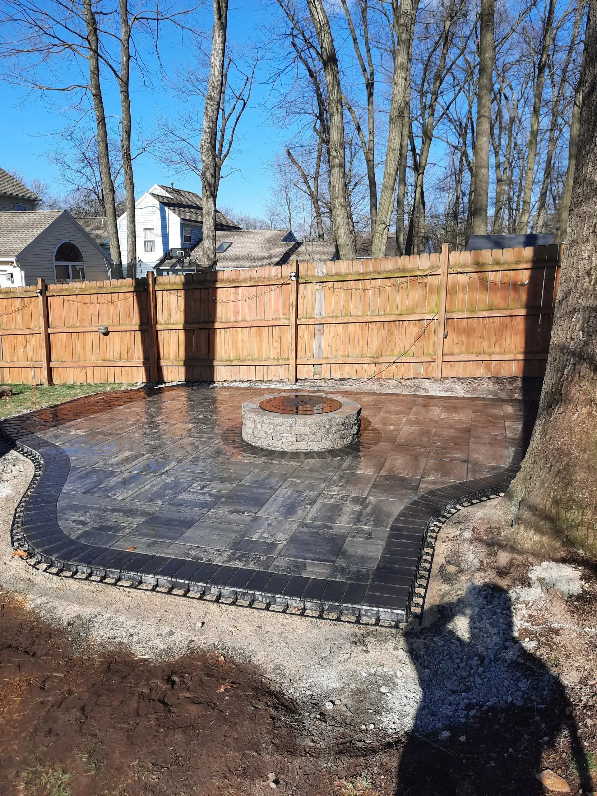 Backyard patio with stamped concrete, a circular fire pit, wooden fence, and leafless trees