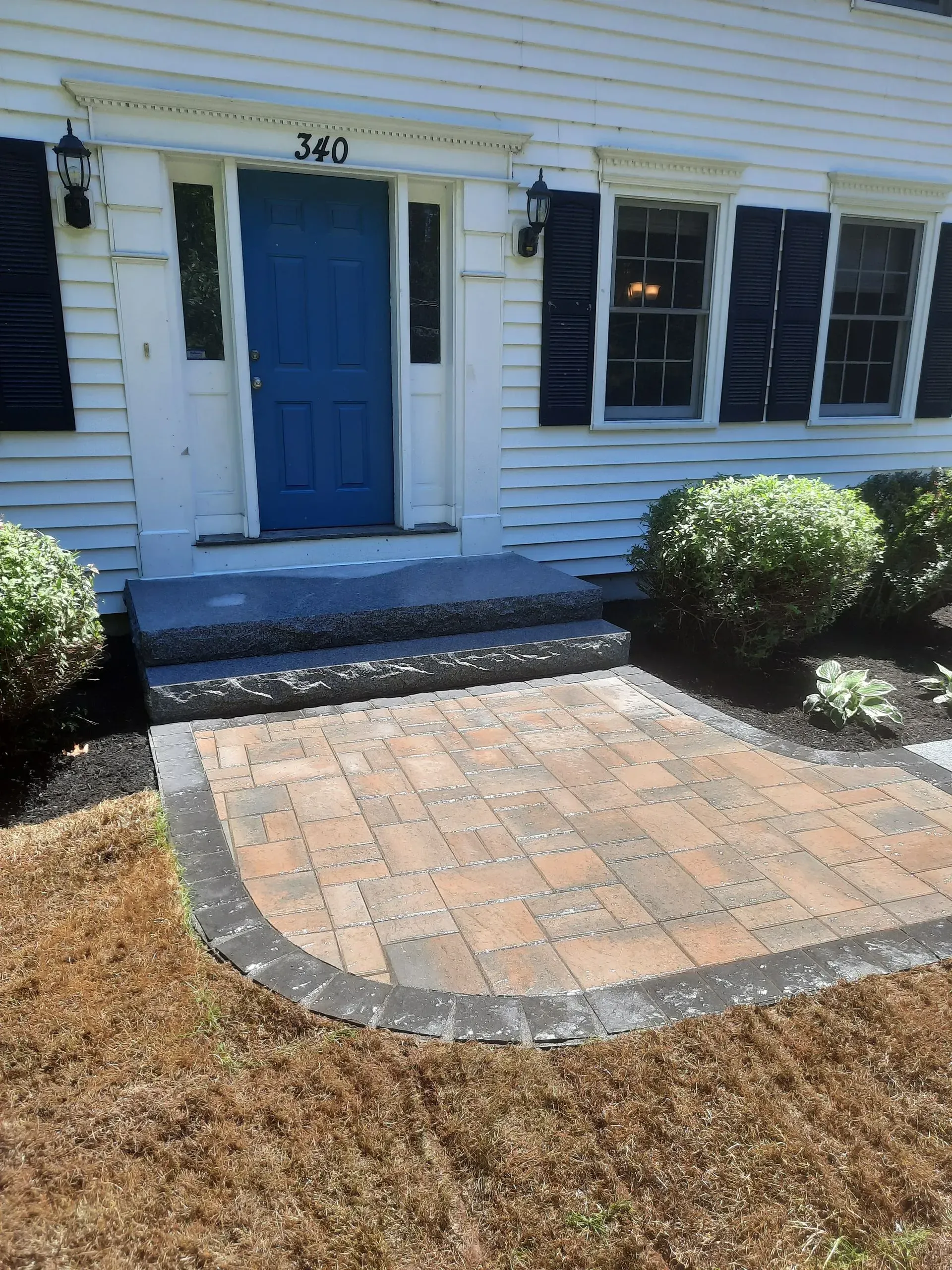 Front entrance with blue door, steps, and brick walkway leading to a white house.