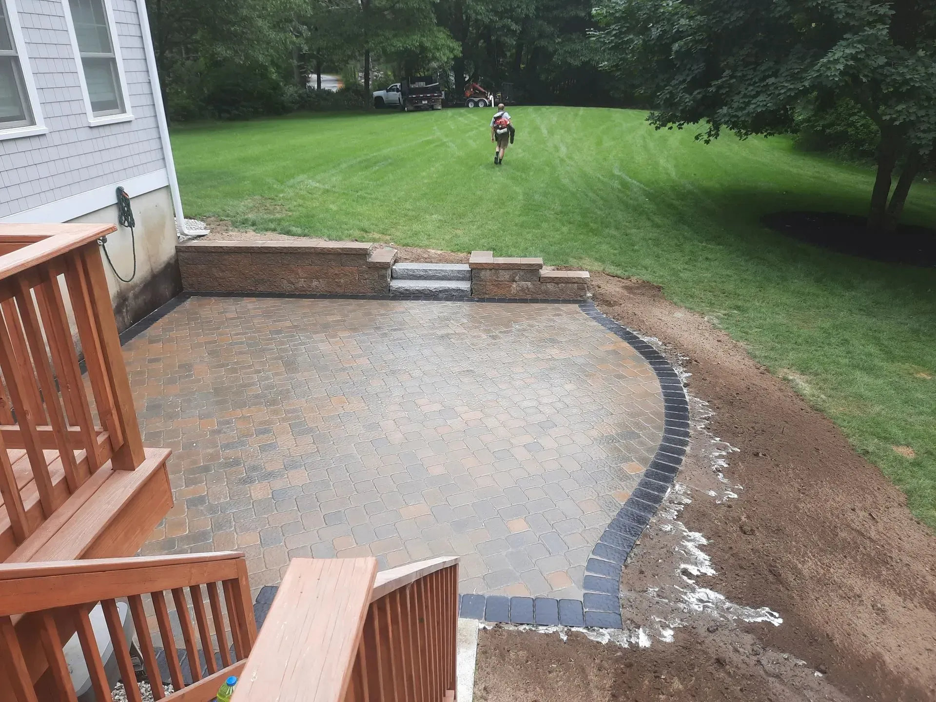Patio under construction with gravel base, curved paver border, and a child running on the lawn nearby