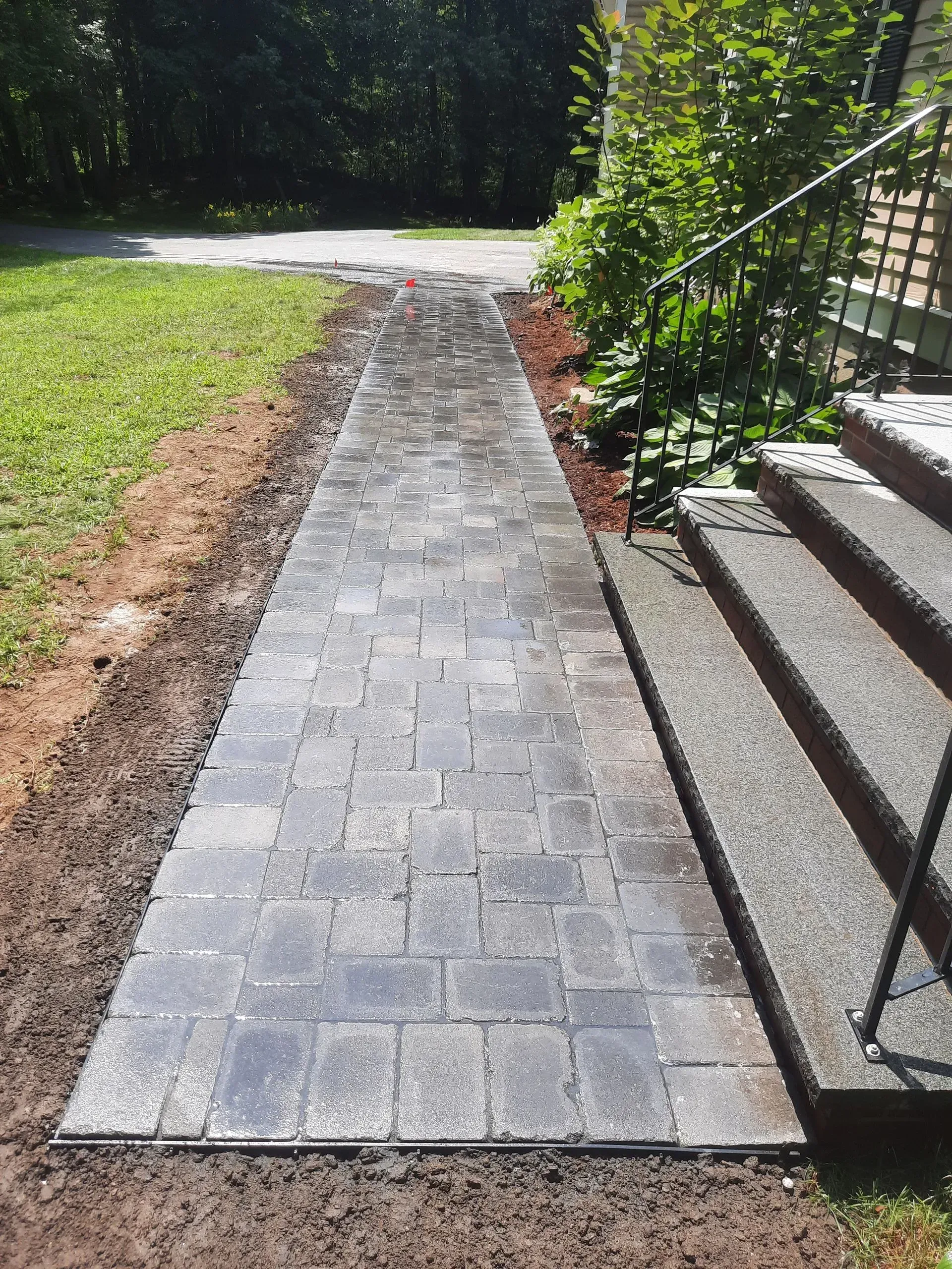 Stone walkway beside lawn and steps, leading to a shaded garden path