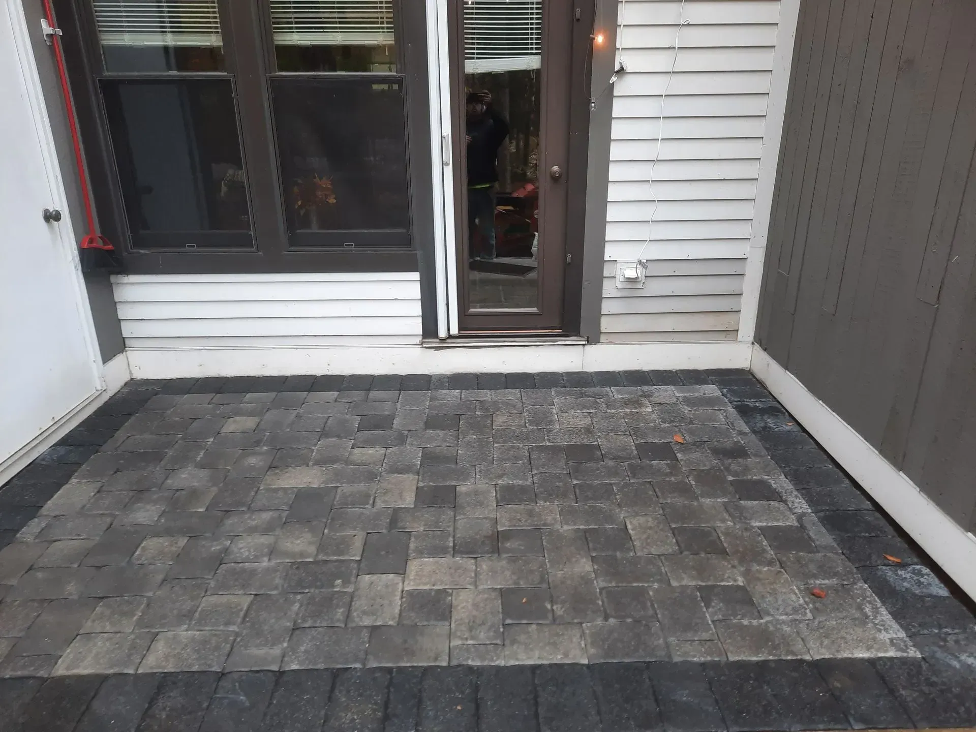 Small gray stone patio with sliding glass doors and siding walls on both sides