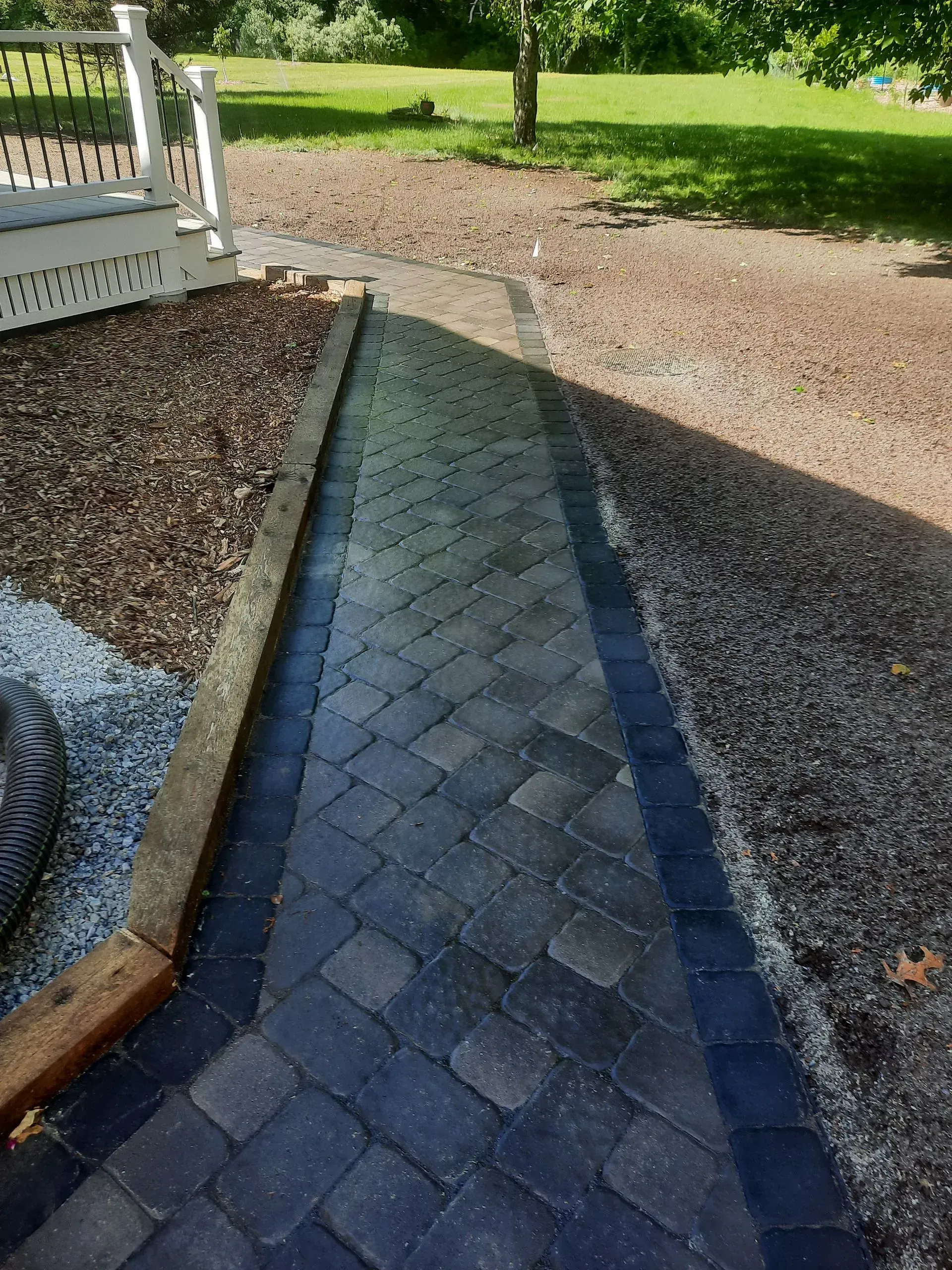 Blue paver walkway leading to a gravel driveway beside a white porch railing