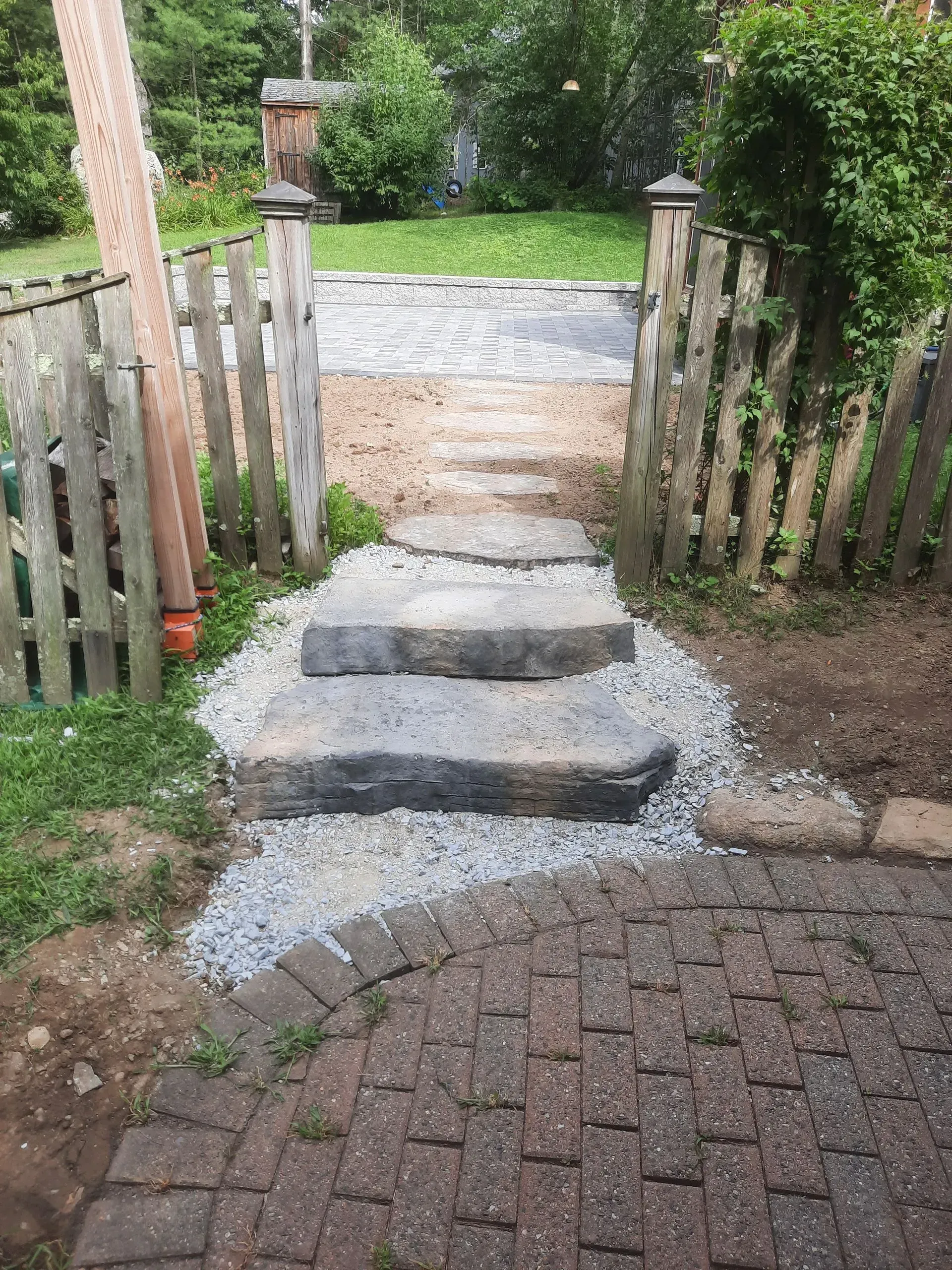 Stepped stone path with a low wooden gate leading from a brick patio into a grassy garden.