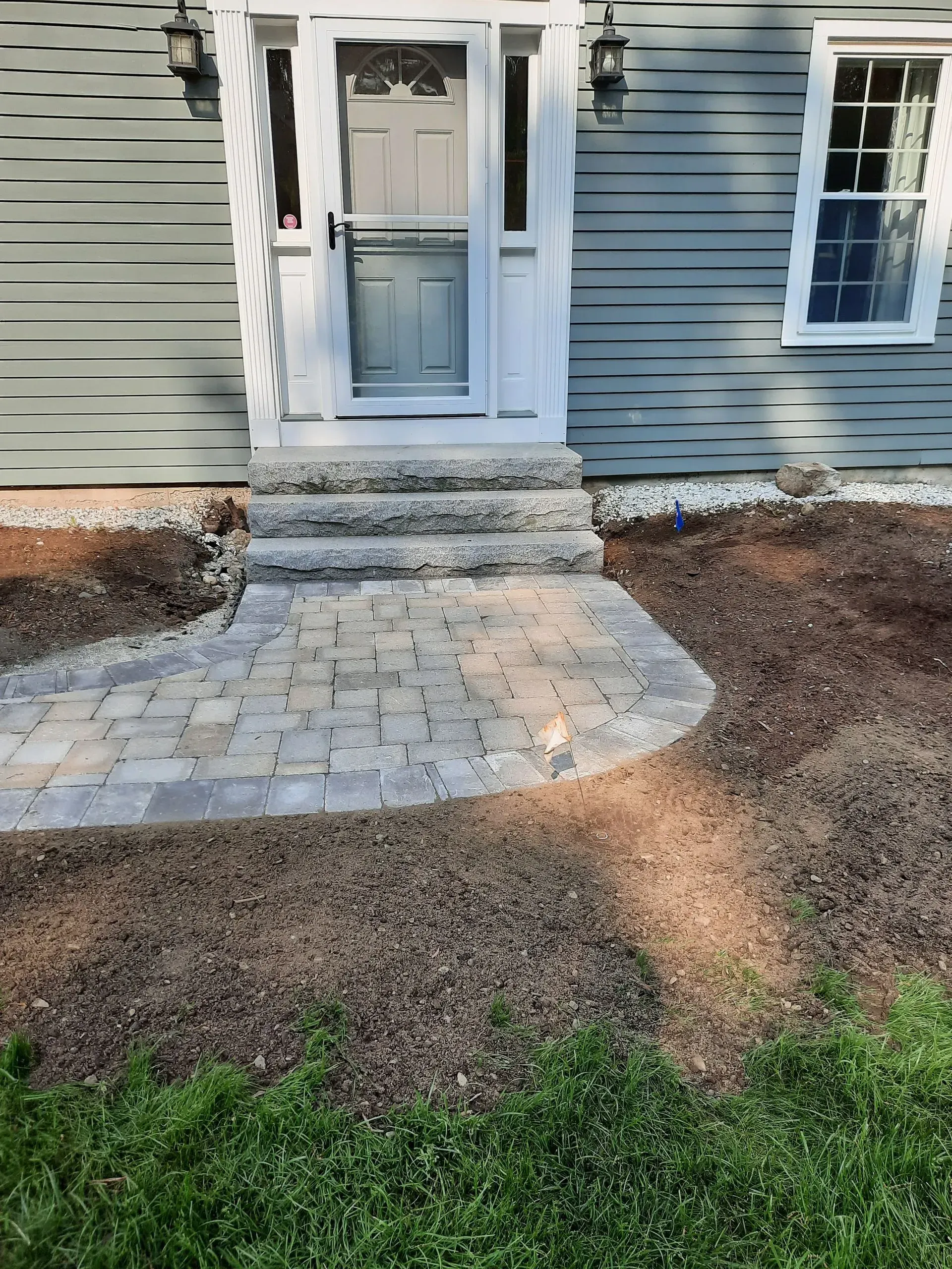 Stone steps lead to a front door on a gray house with a small paved walkway and gravel yard.