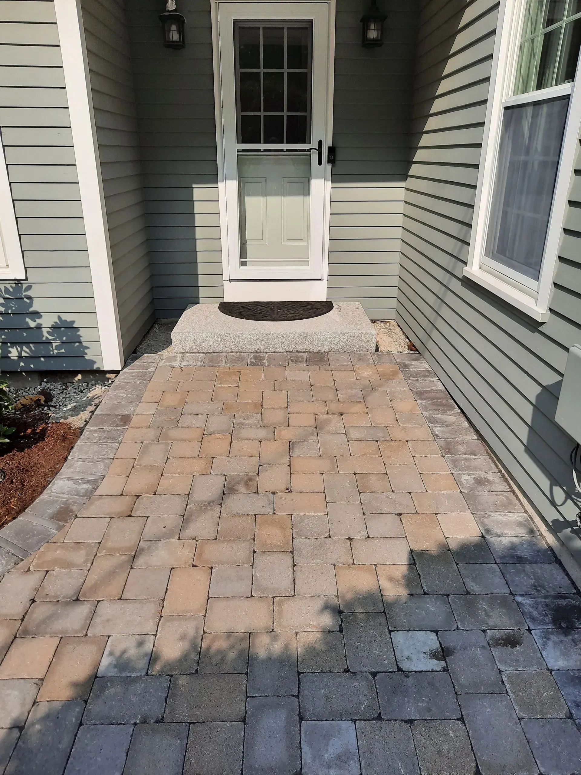 Brick walkway leading to a white front door between gray house siding and windows