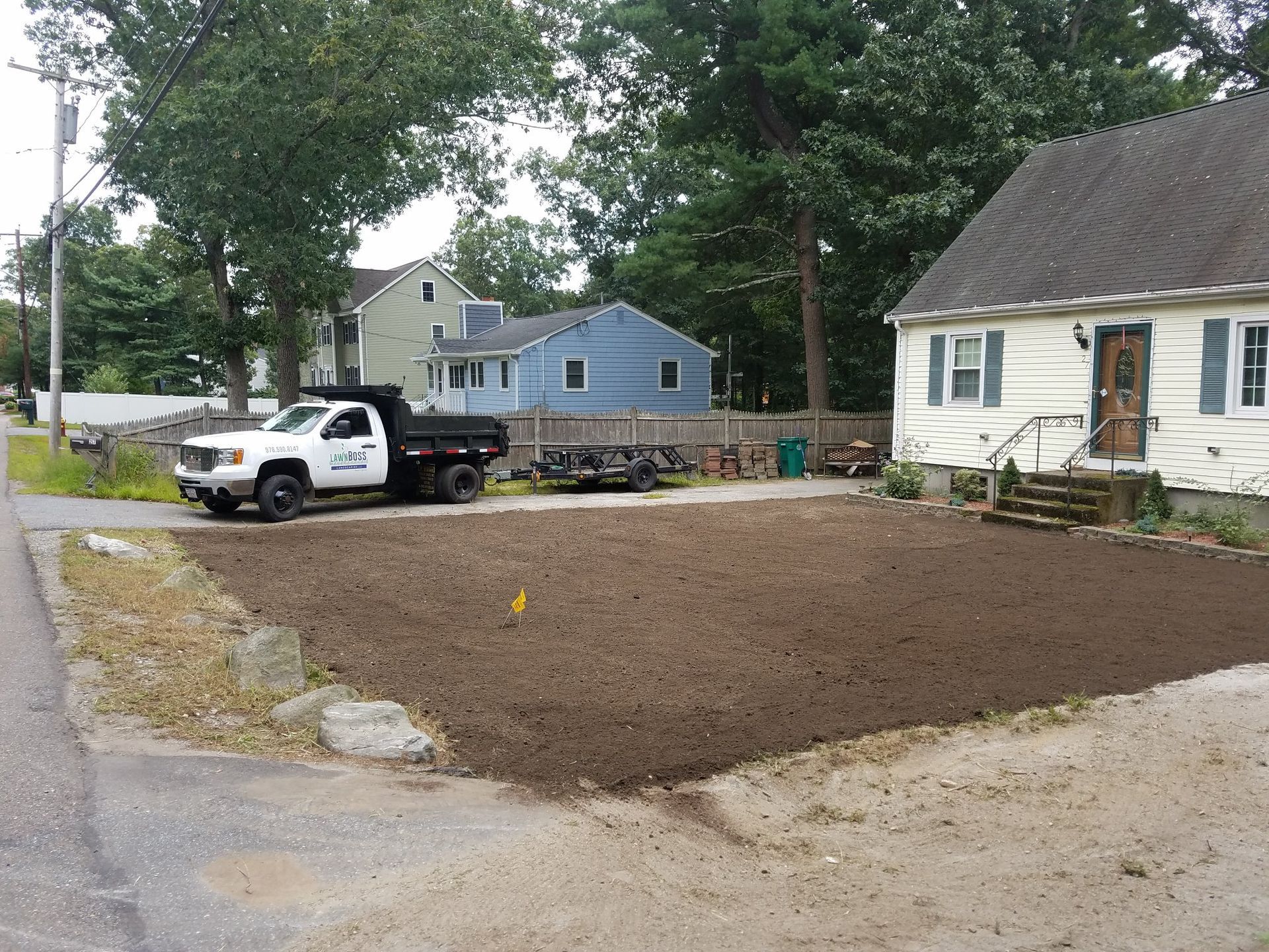 Small front yard with fresh brown dirt, a white pickup truck, and houses along a quiet street.