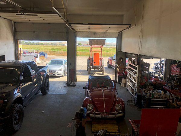 A red beetle is parked in a garage next to a tractor.